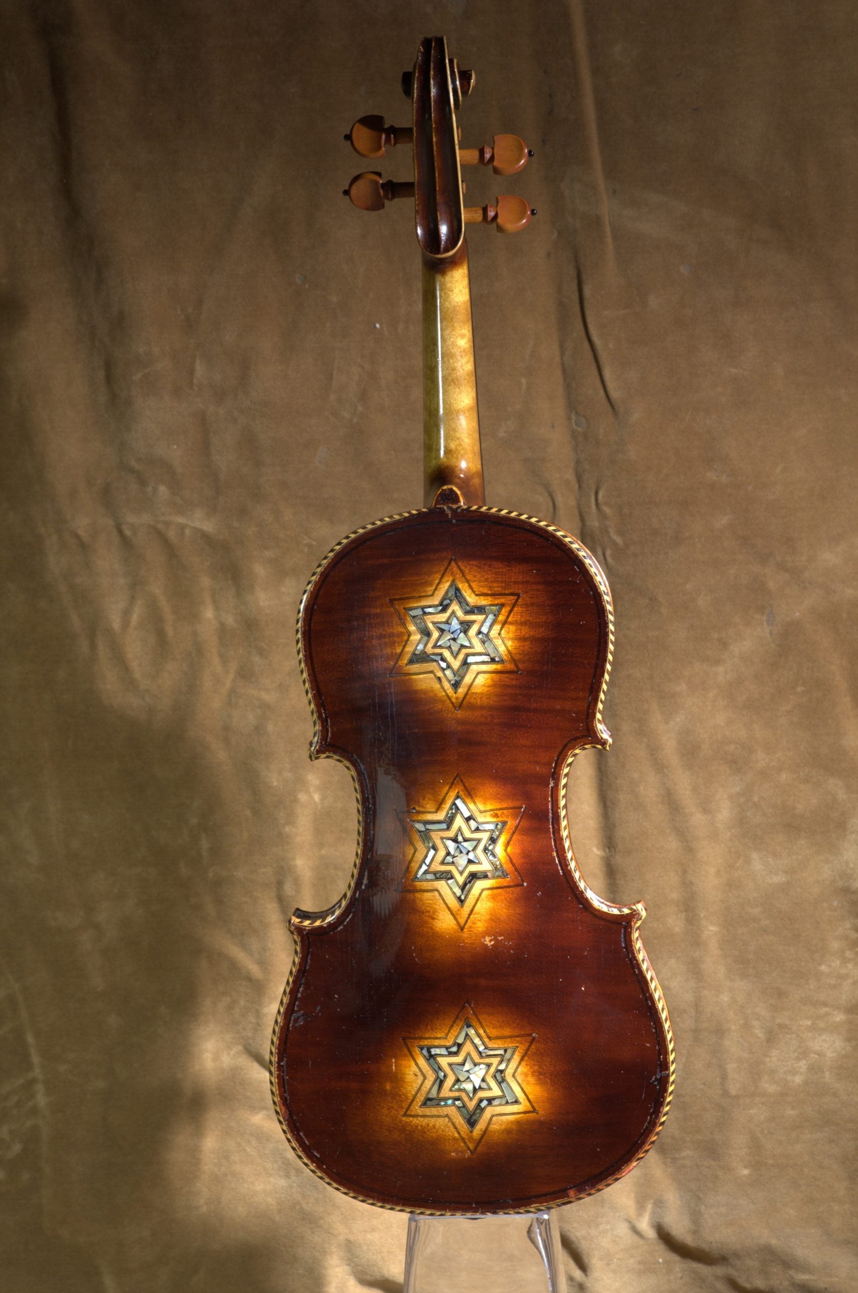 A violin with three star-shaped inlays on its back, resting on a brown fabric surface.