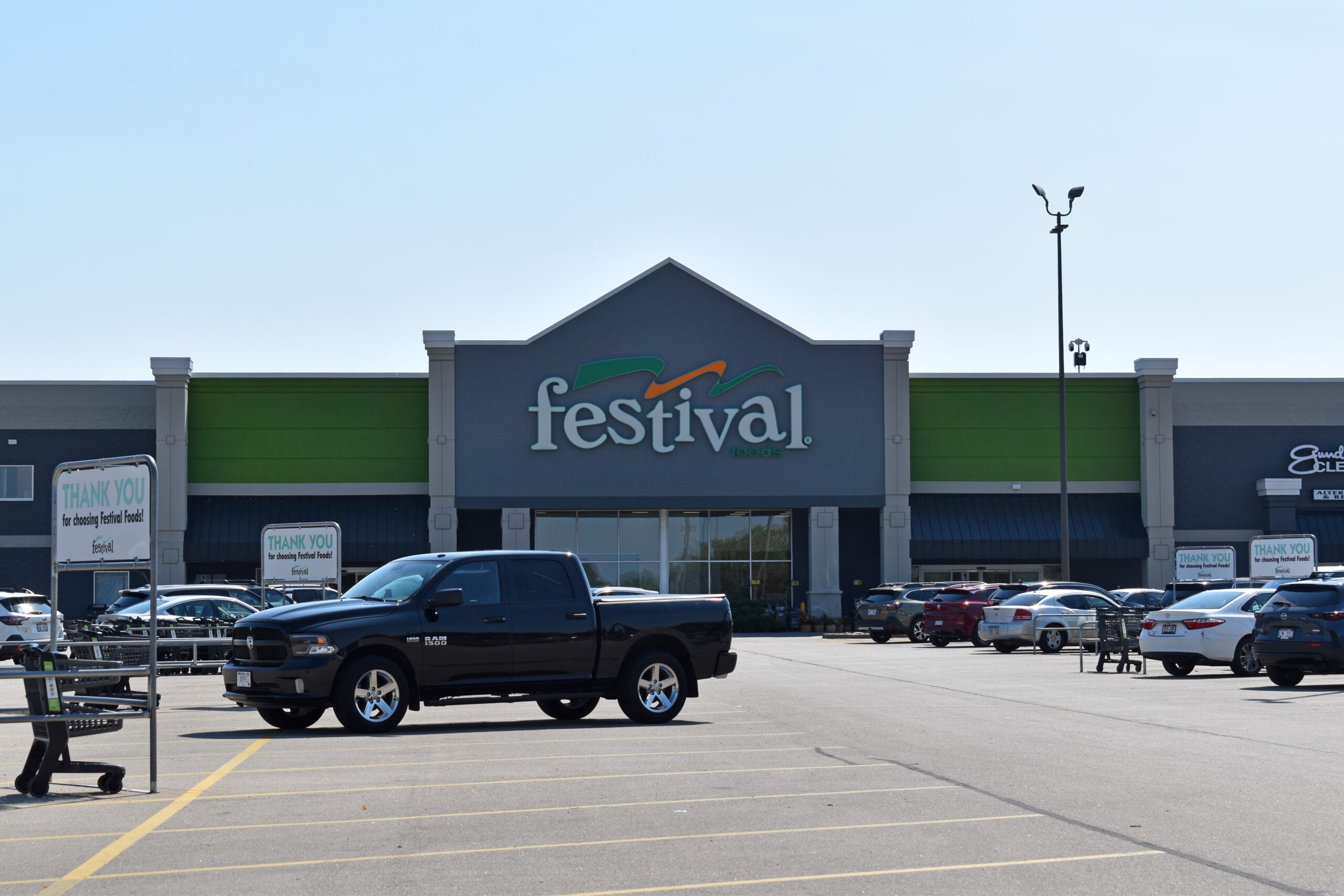 A black pickup truck is parked in front of a Festival Foods grocery store, with several other cars and shopping carts visible in the parking lot.