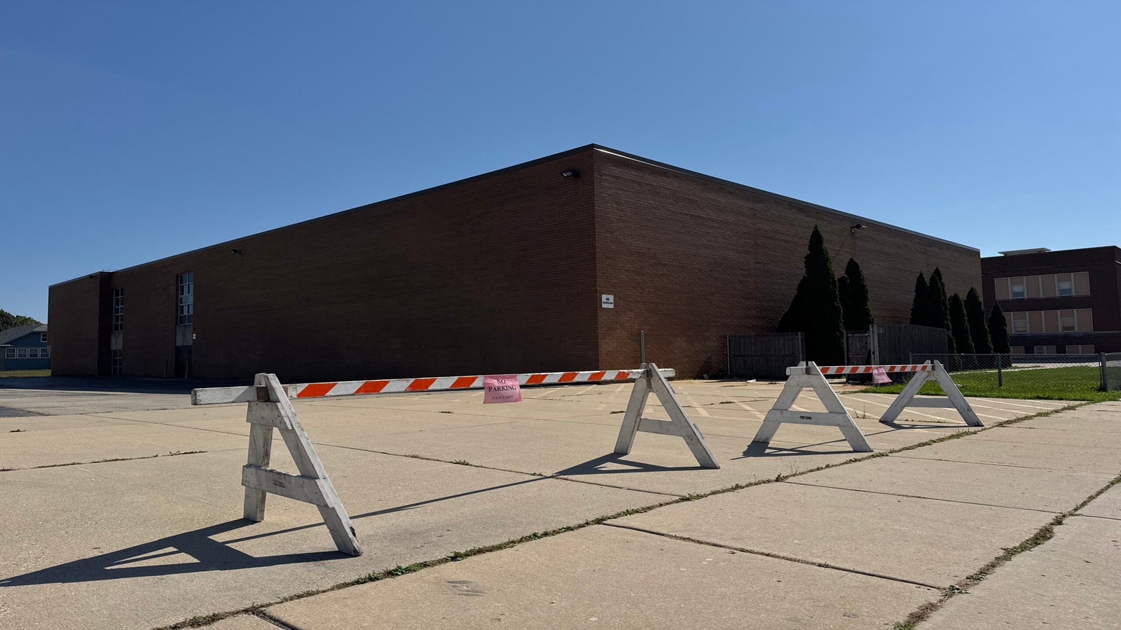 A brick building with no windows on one side is blocked off by striped barricades on a sunny day.