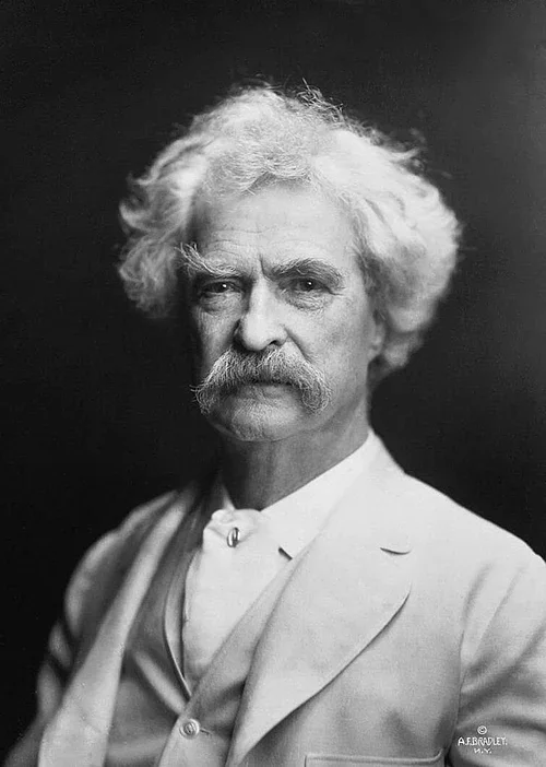 Black-and-white portrait of an older man with white hair and a large mustache, wearing a light-colored suit and vest, facing the camera against a dark background.