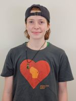 A person with short hair wearing a backward cap and a dark T-shirt with a heart and state graphic stands in front of a plain light-colored wall.