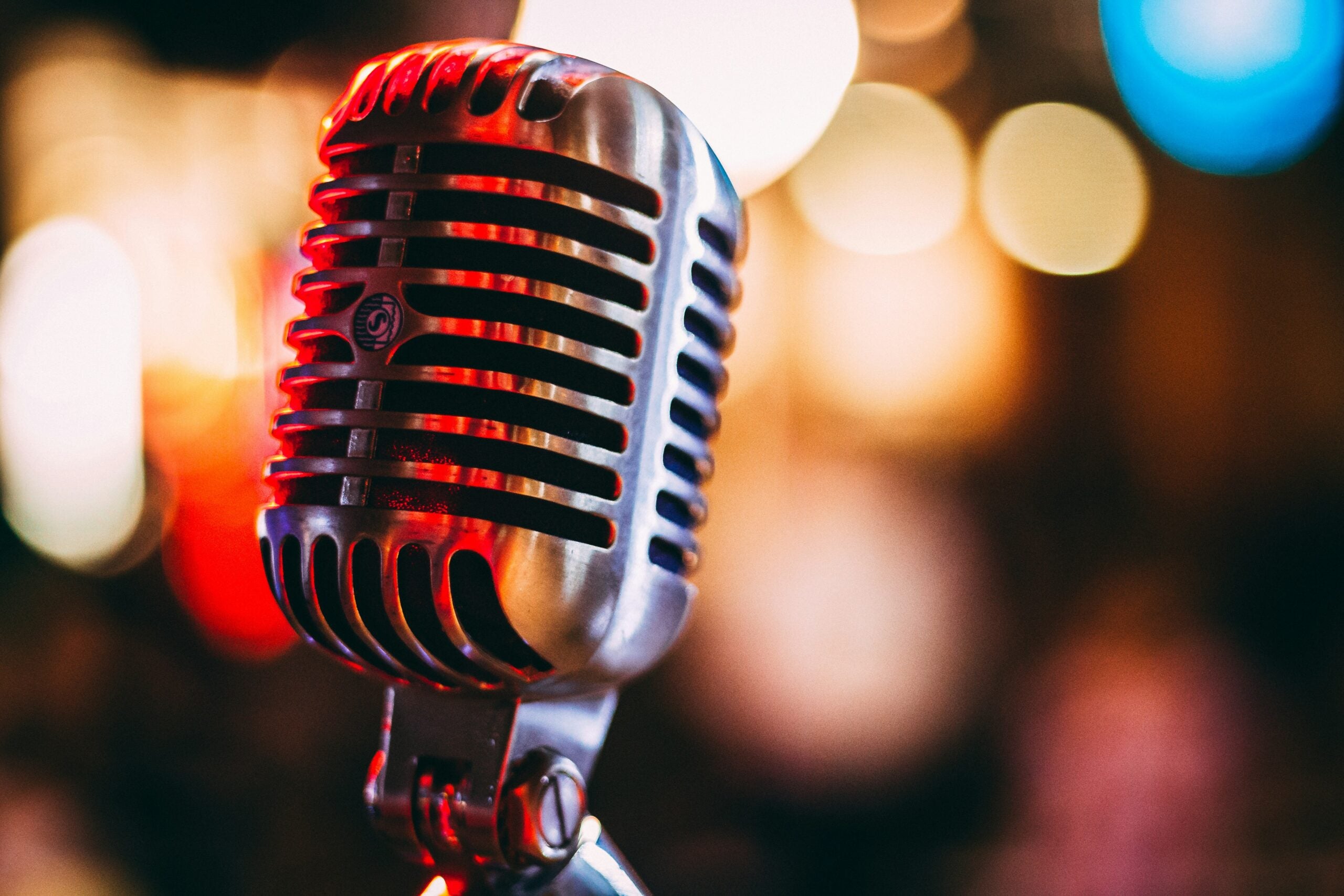 Close-up of a vintage silver microphone with blurred colorful lights in the background.
