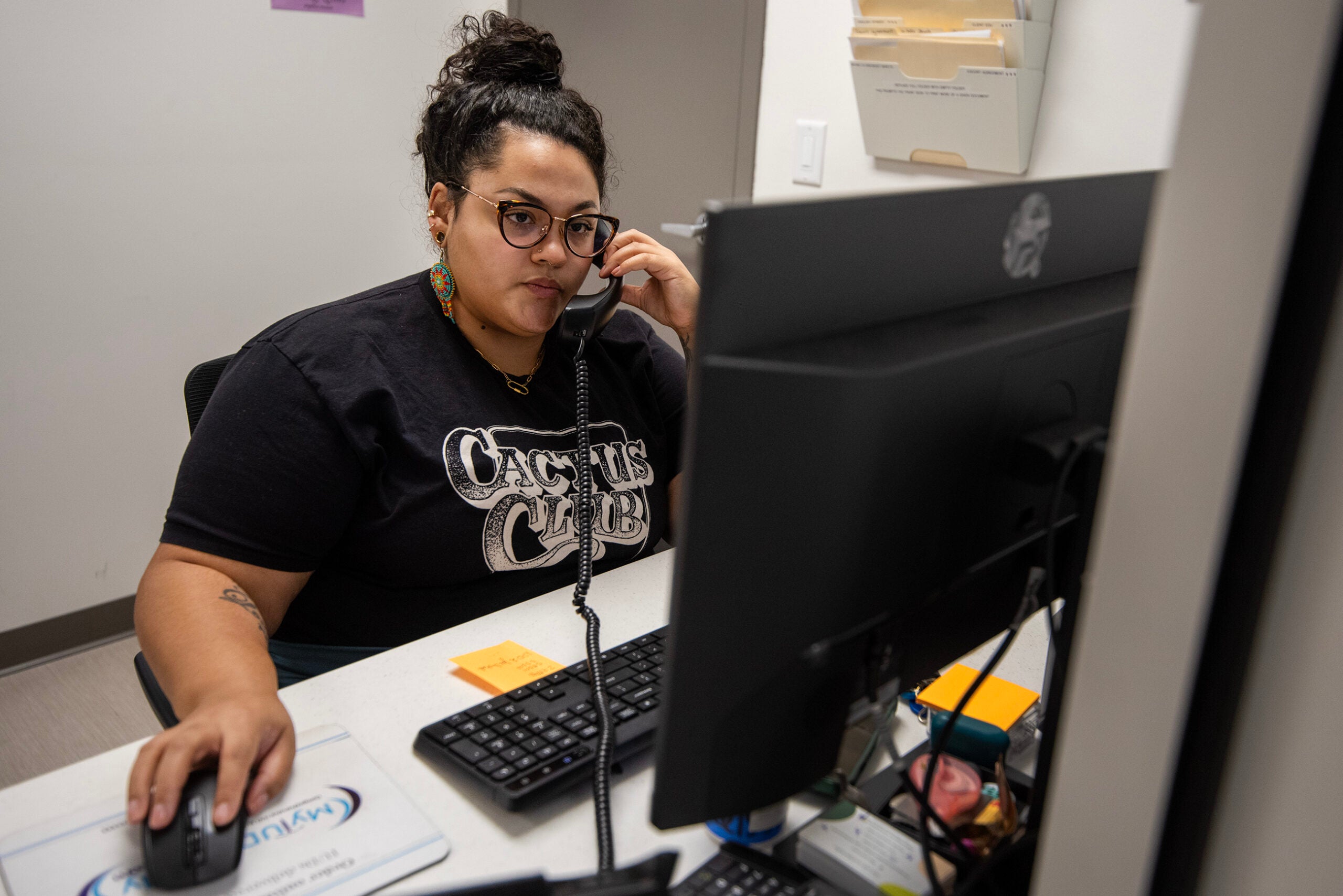 A person sits at a desk using a computer and talking on the phone in an office setting.