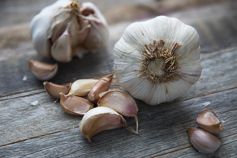 Two whole heads of garlic and several loose garlic cloves are arranged on a rustic wooden surface.
