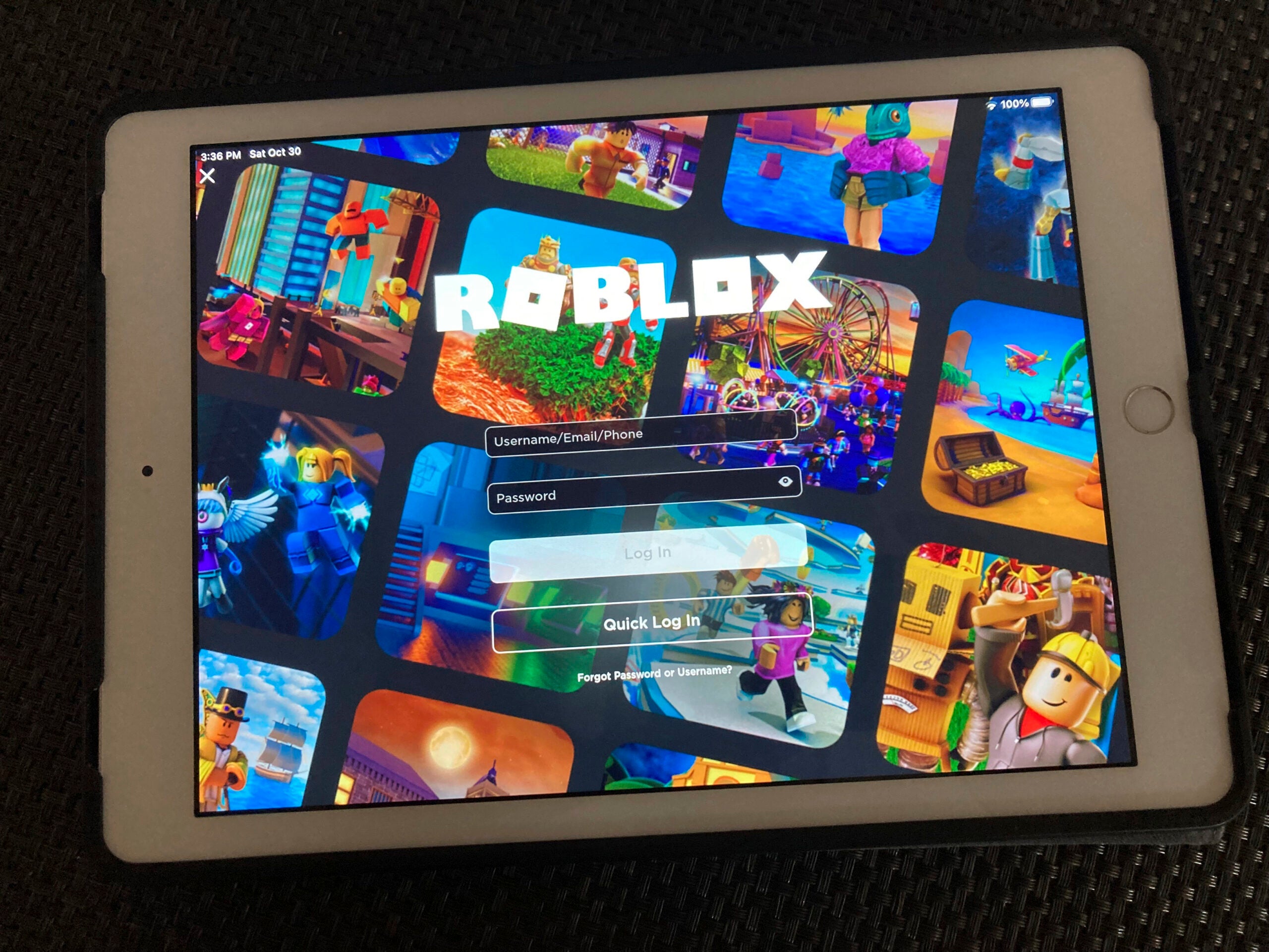 A tablet displays the Roblox login screen, featuring a collage of animated game scenes in the background.