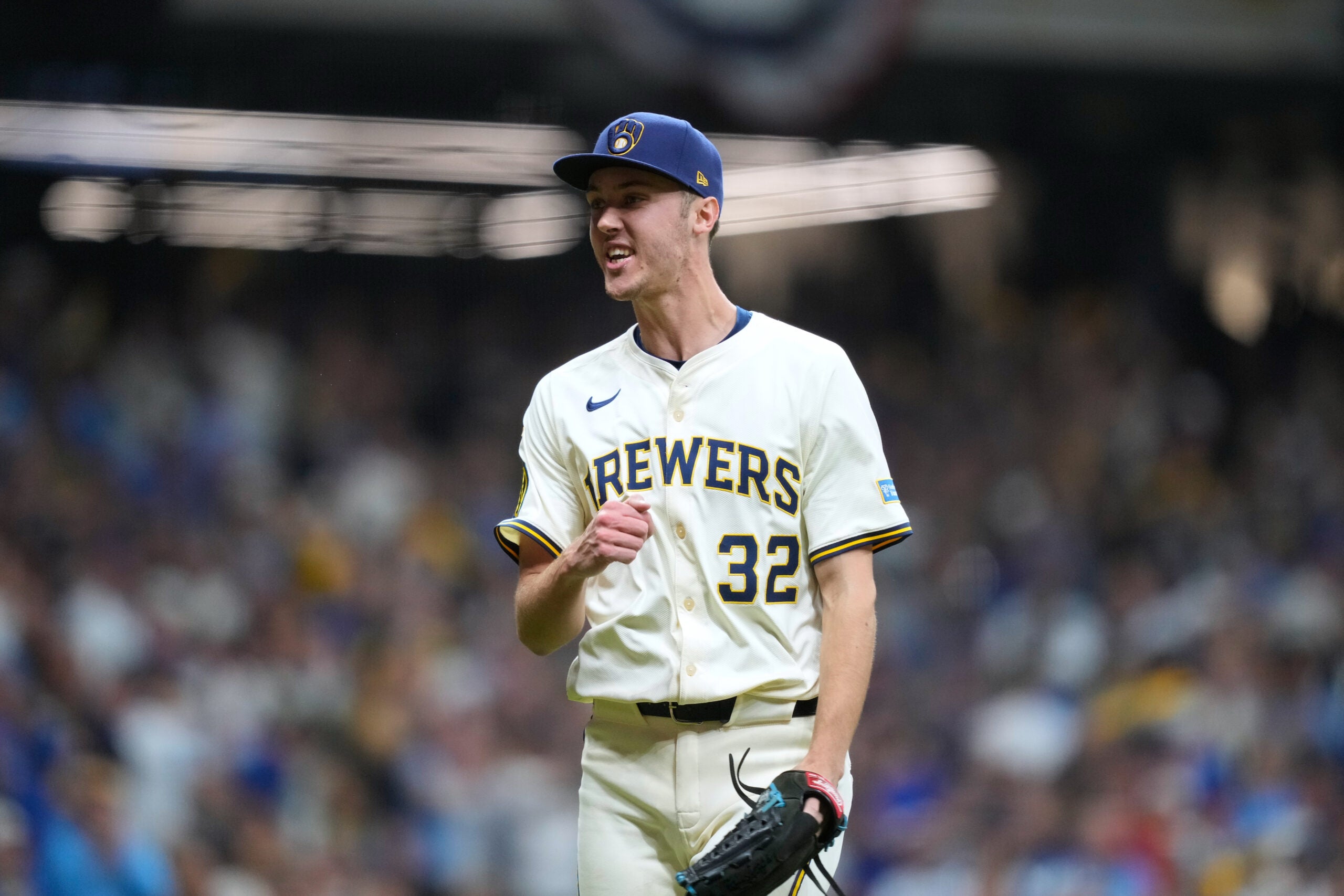A baseball player in a Milwaukee Brewers uniform, number 32, stands on the field holding a glove, with a crowd in the background.