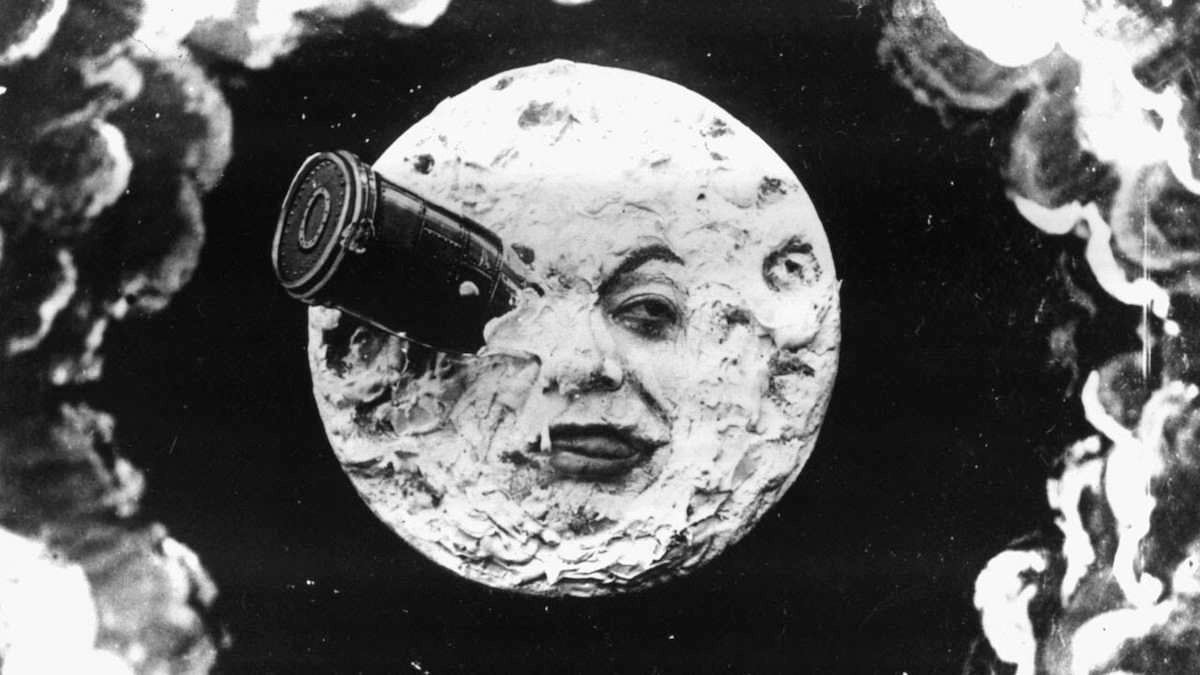 A large, human-like face is depicted on the moon, which has a rocket lodged in one eye; black and white, surreal imagery.