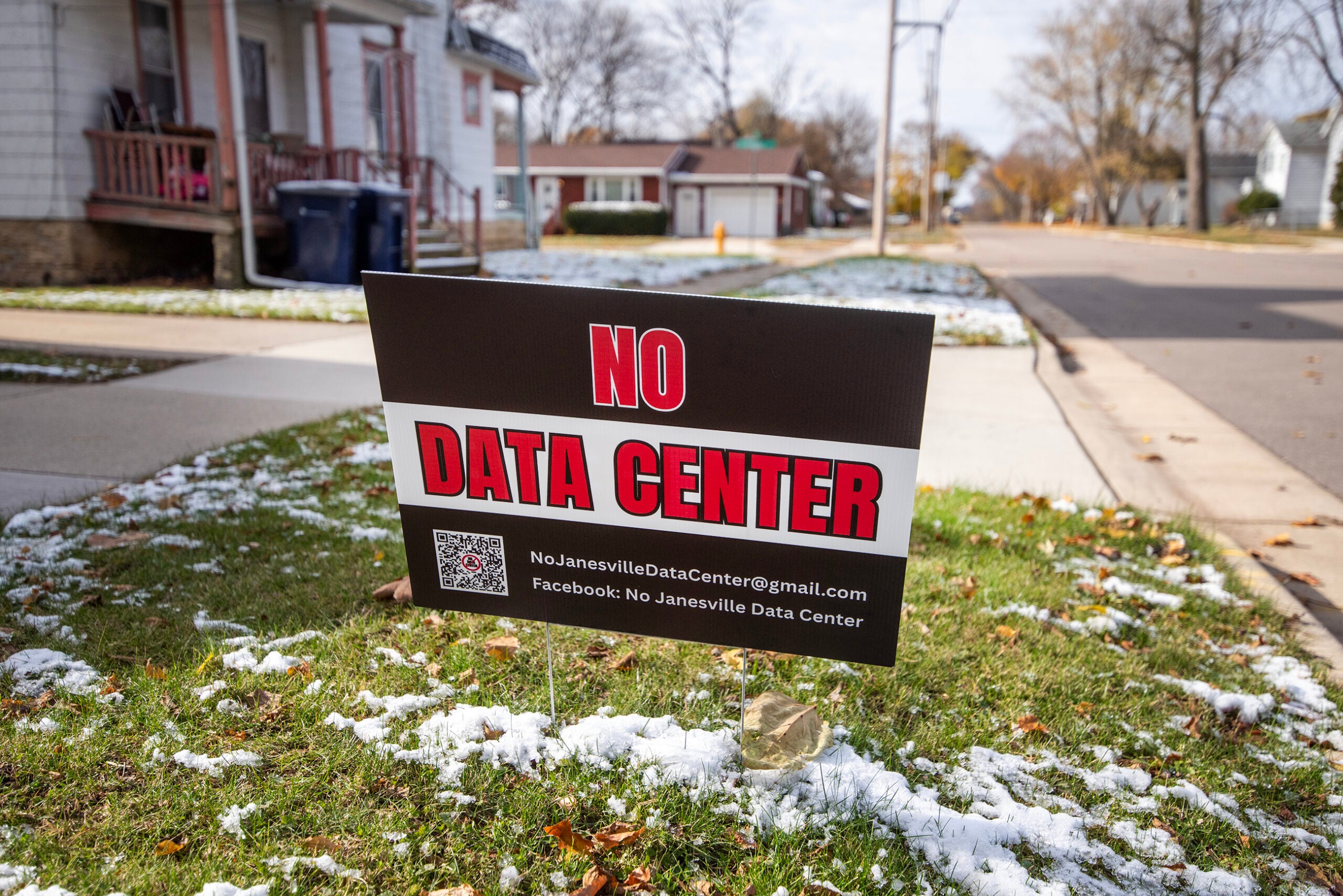 A yard sign on a residential lawn reads NO DATA CENTER with contact information and a QR code, indicating opposition to a proposed data center in the neighborhood.