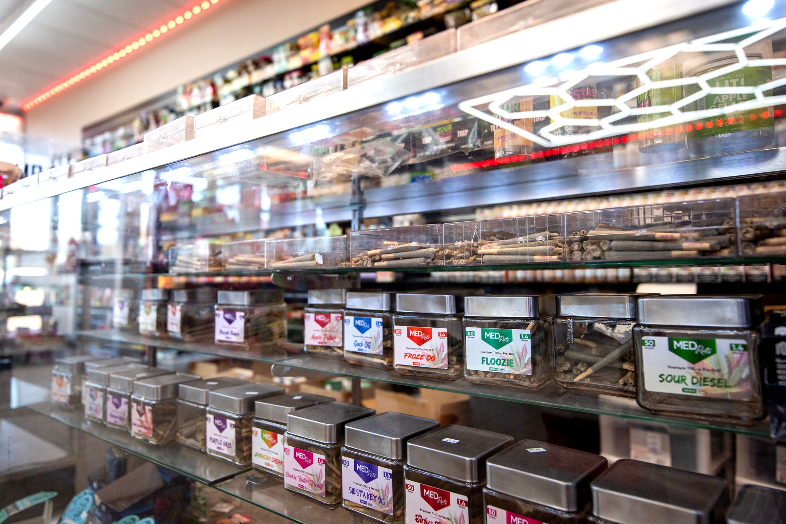 Glass display case in a store containing pre-rolled joints on the upper shelves and labeled cannabis containers on the lower shelves.