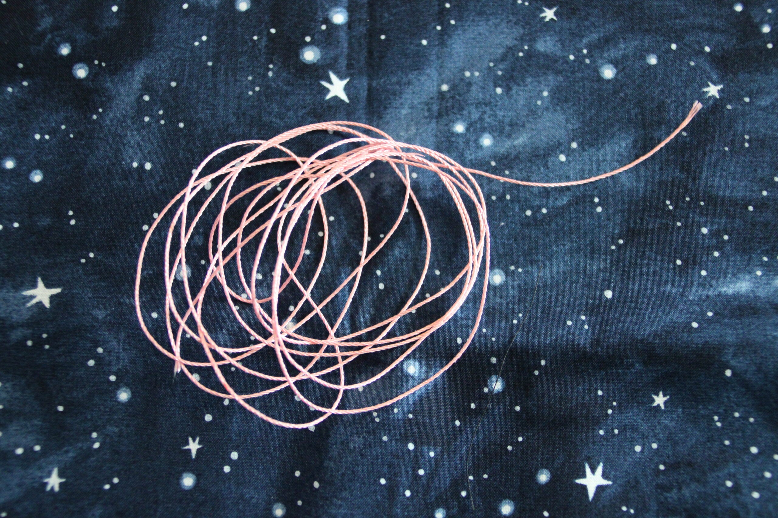 A bundle of pink string is loosely coiled on a dark blue fabric with a starry night sky pattern.