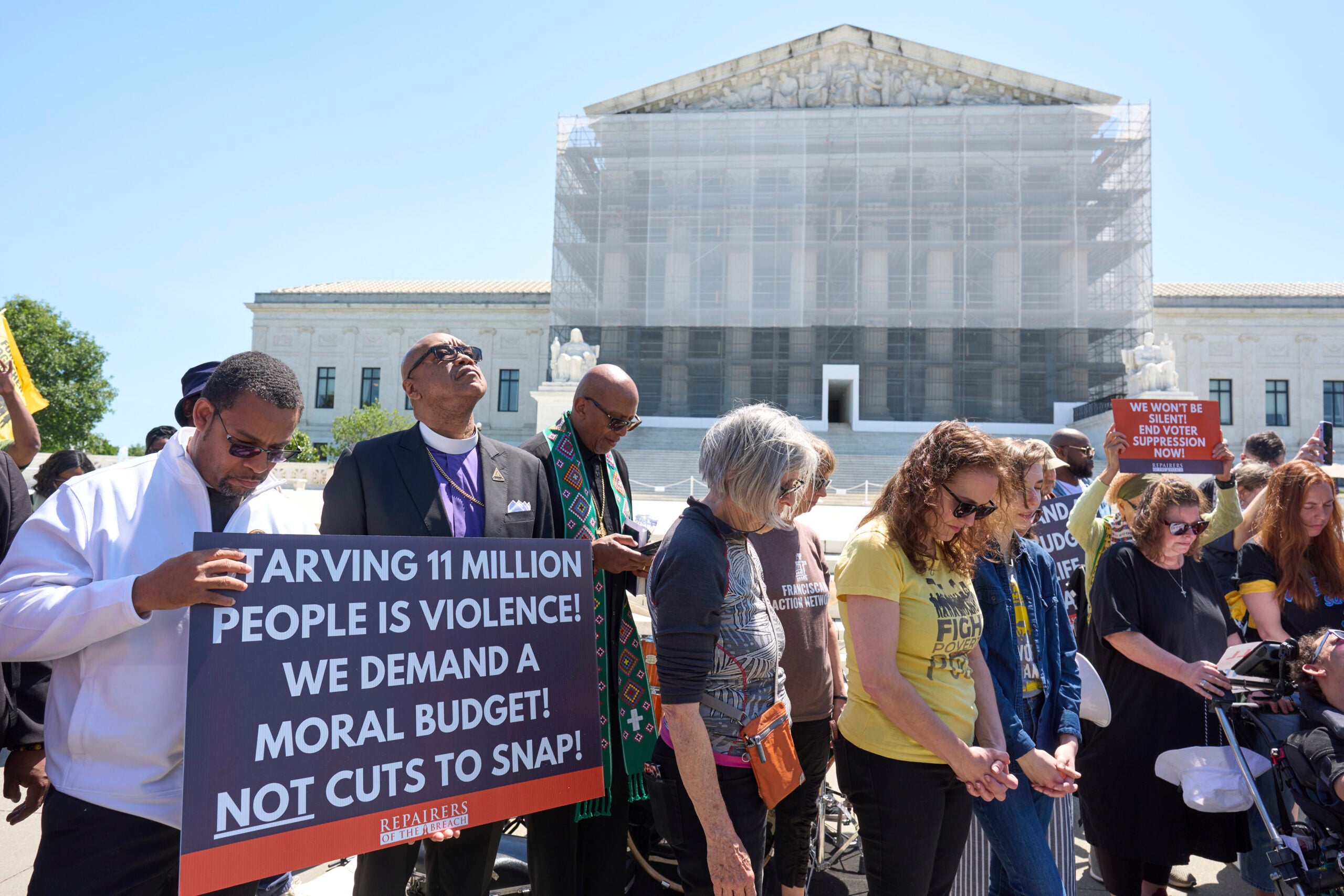 A group of protesters stand in front of a government building holding signs demanding protection for SNAP benefits and calling for a moral budget.
