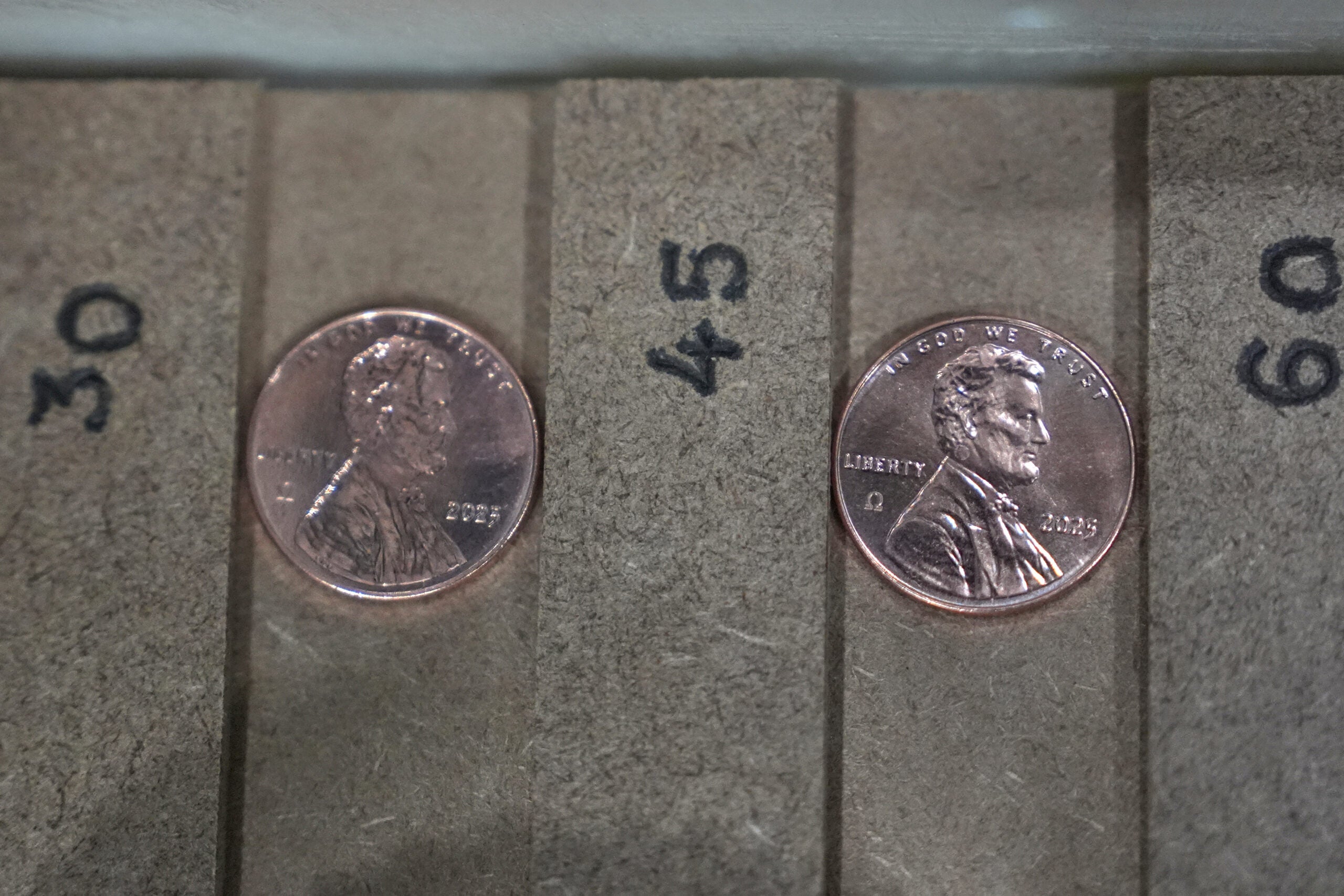 Two US pennies dated 2023 are placed in separate slots labeled 30 and 45 on a cardboard coin sorting tray.