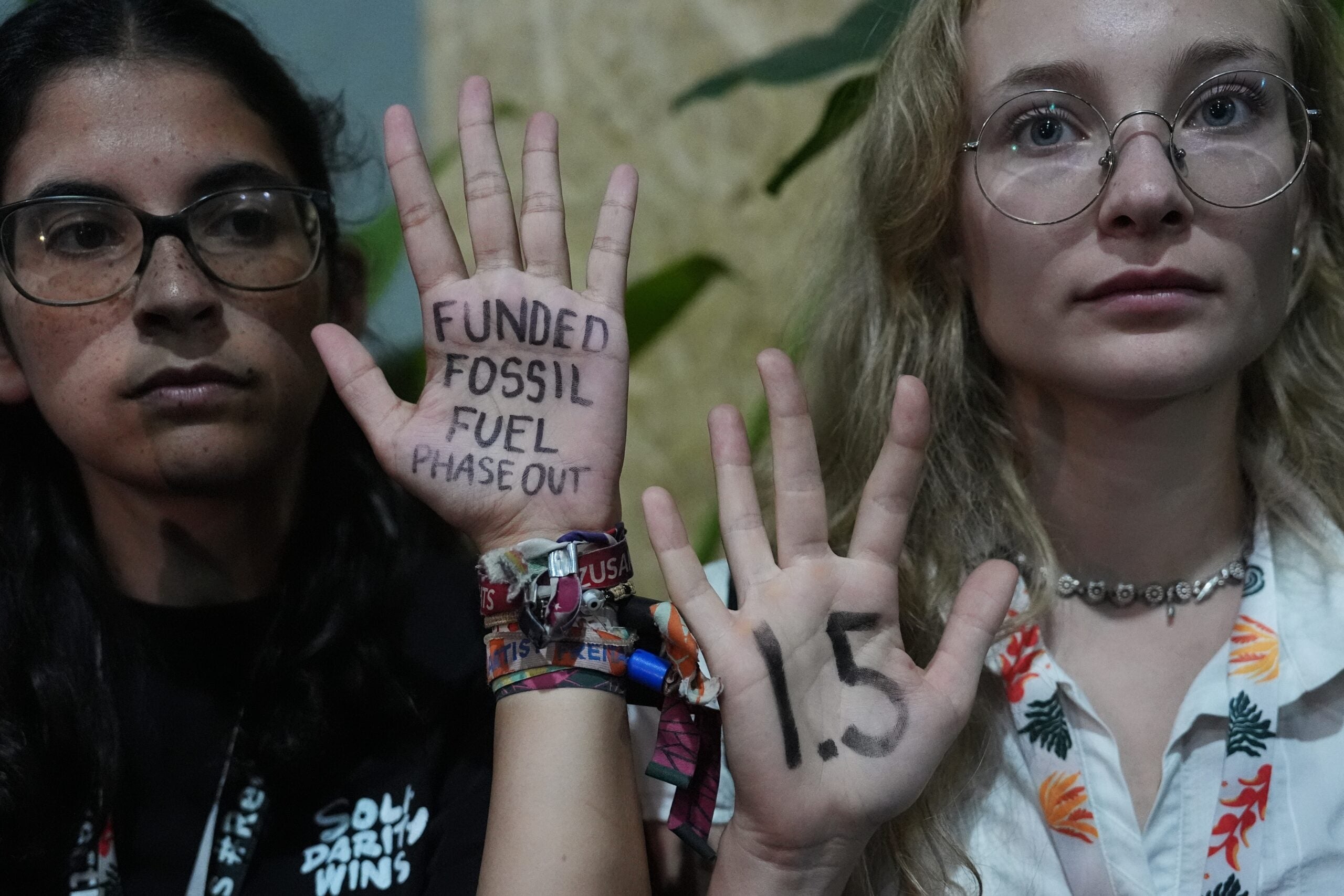 Two people hold up their hands with messages written on their palms: FUNDED FOSSIL FUEL PHASE OUT and 1.5, likely in reference to climate action targets.