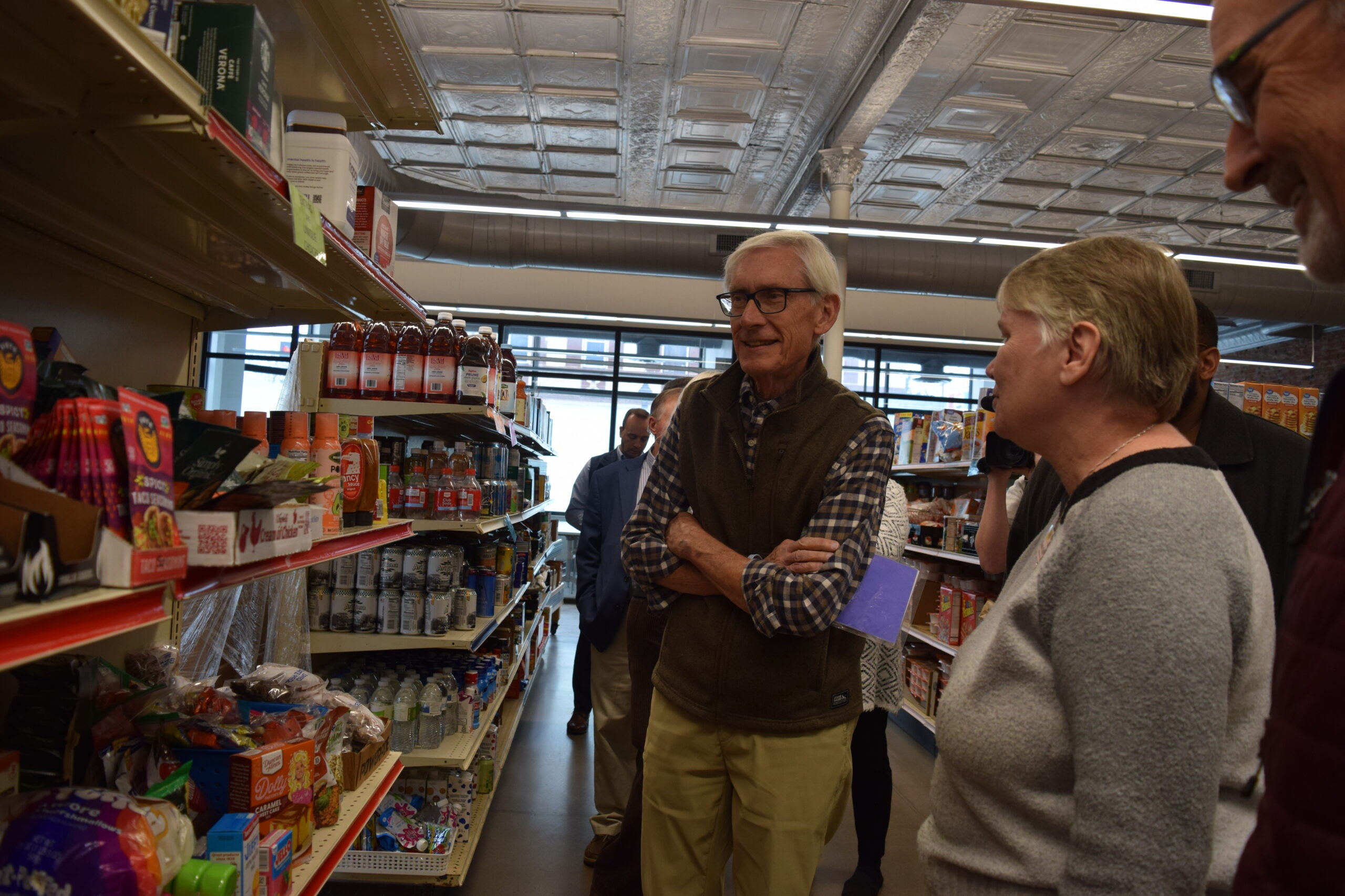 A group of people stand and look at items on store shelves inside a grocery store.