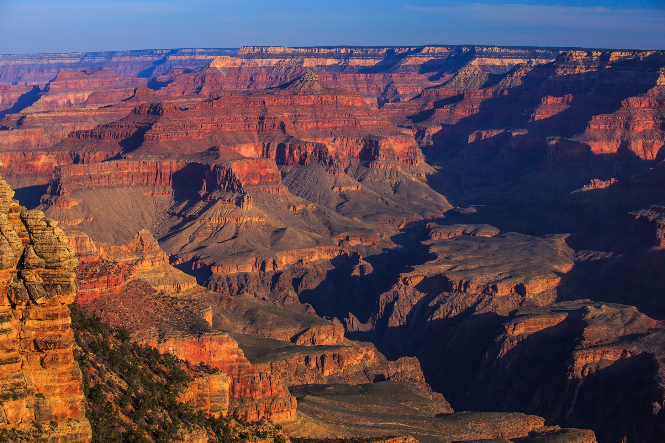 View of the Grand Canyon with layered red rock formations, steep cliffs, and deep valleys under a clear blue sky.