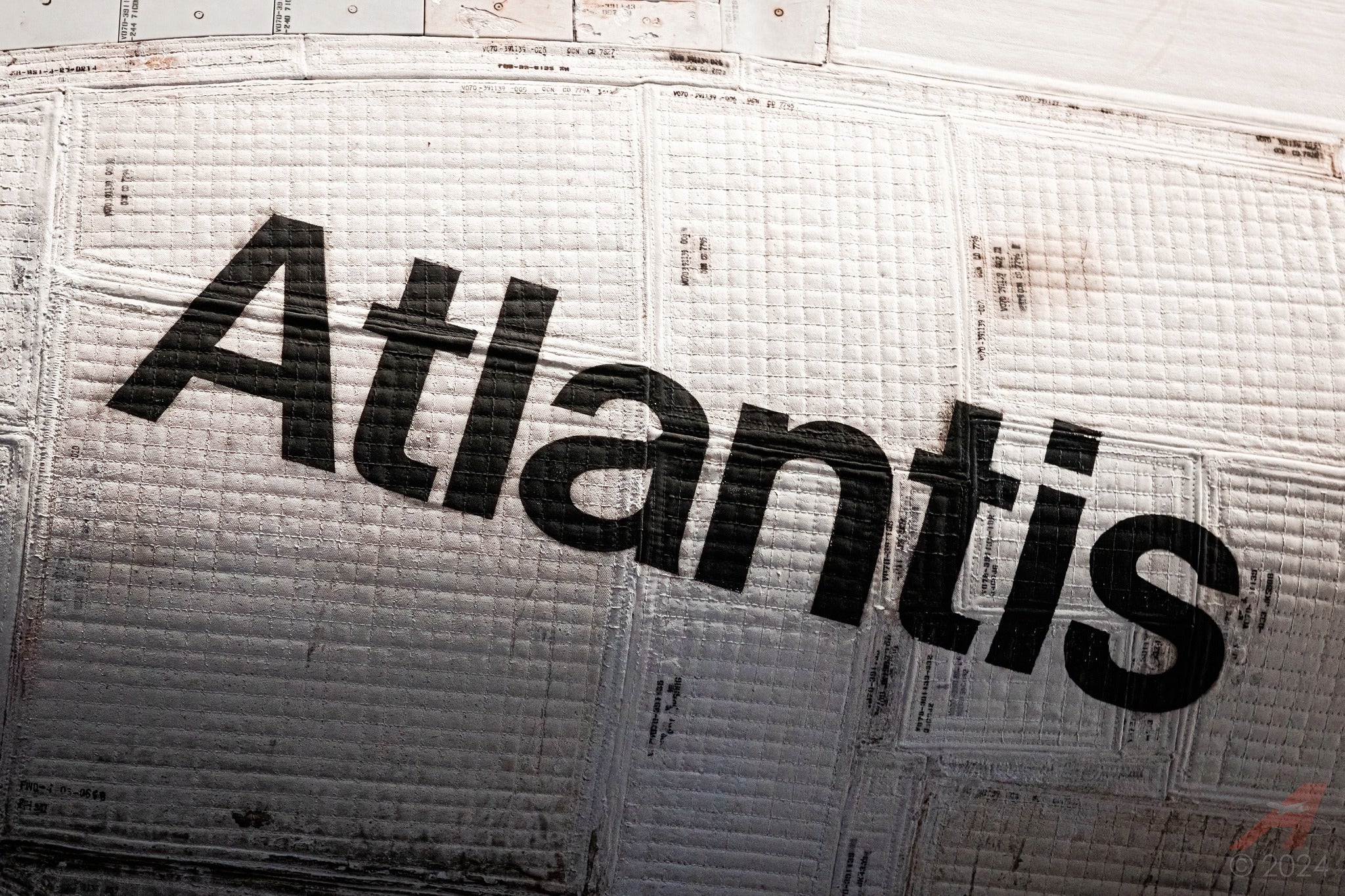 Close-up view of the space shuttle Atlantis name written in black letters on its white, textured exterior tiles.