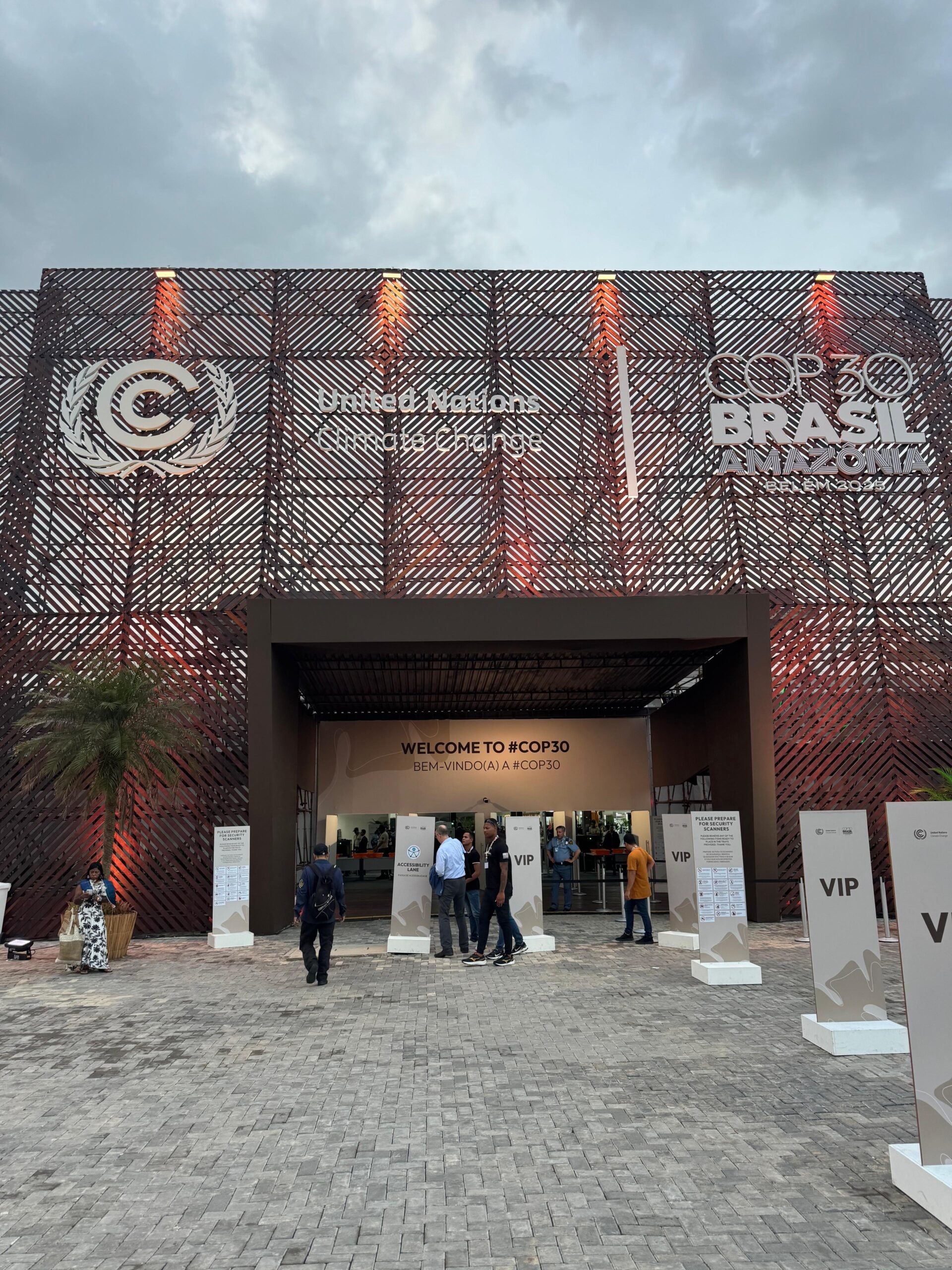 Exterior view of the United Nations COP30 event entrance in Brazil, with people entering under signage for attendees and VIP areas.