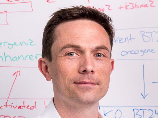 A man in a white shirt stands in front of a whiteboard covered with scientific diagrams and colorful handwritten notes.