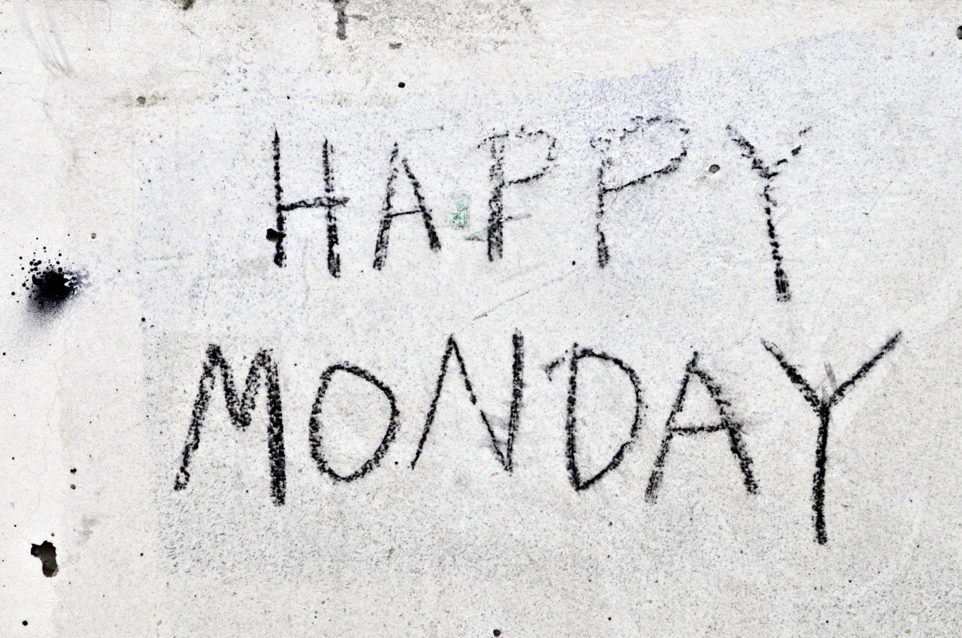 Text HAPPY MONDAY written in black on a rough, gray concrete wall.