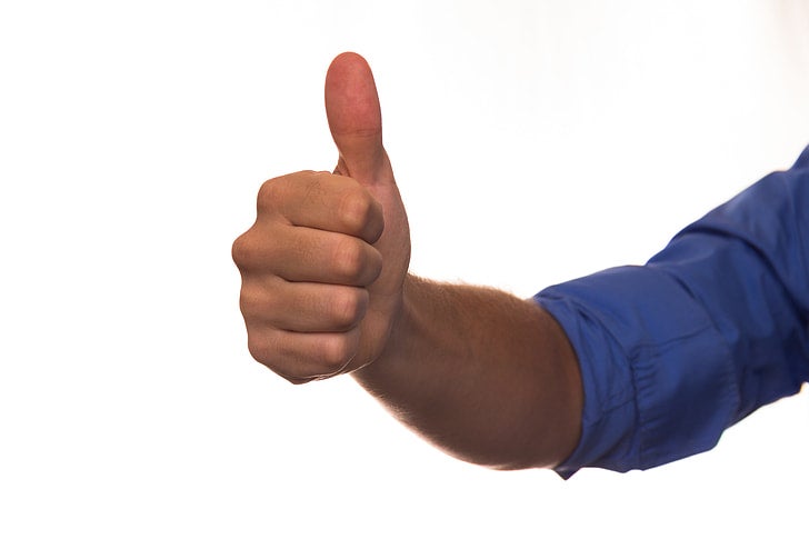 A person wearing a blue long-sleeve shirt gives a thumbs-up gesture against a plain white background.