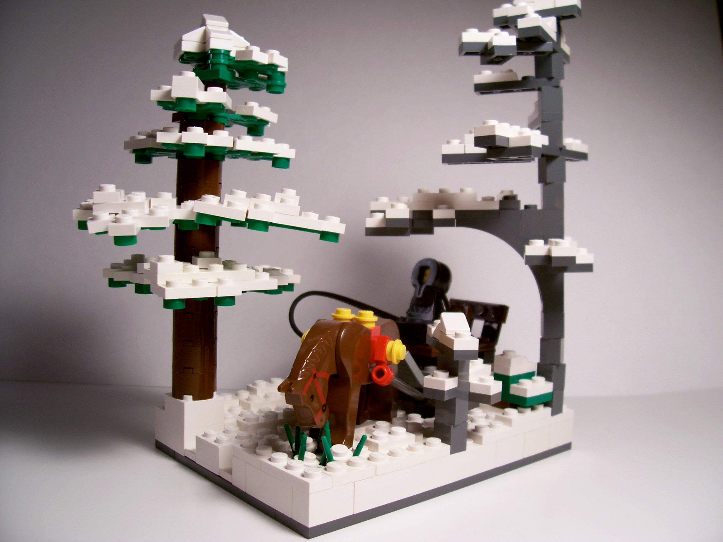 LEGO scene depicting a hooded figure riding a brown horse through a snowy landscape with two snow-covered trees.