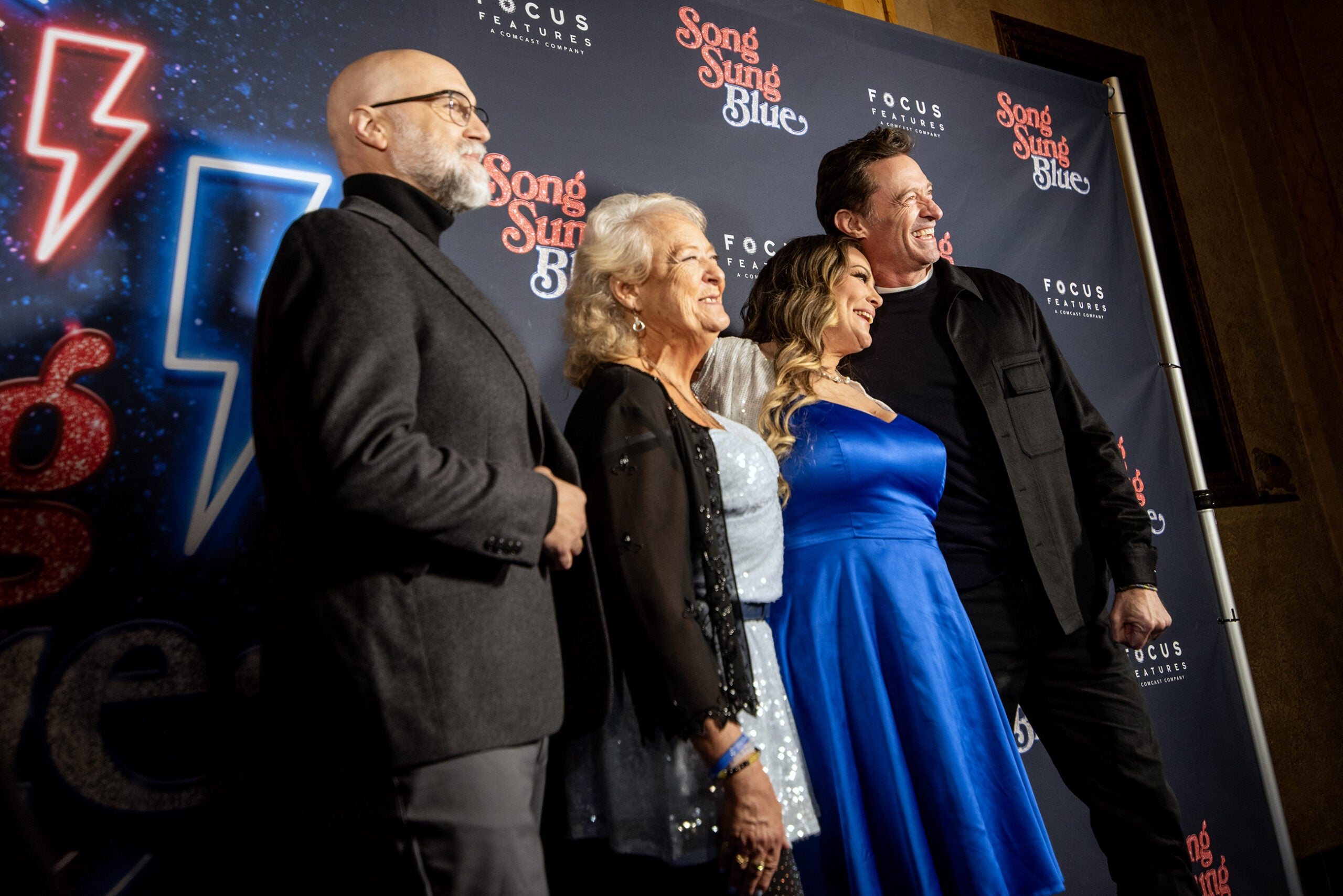 Four people pose together on a red carpet in front of a backdrop for Song Sung Blue and Focus Features.