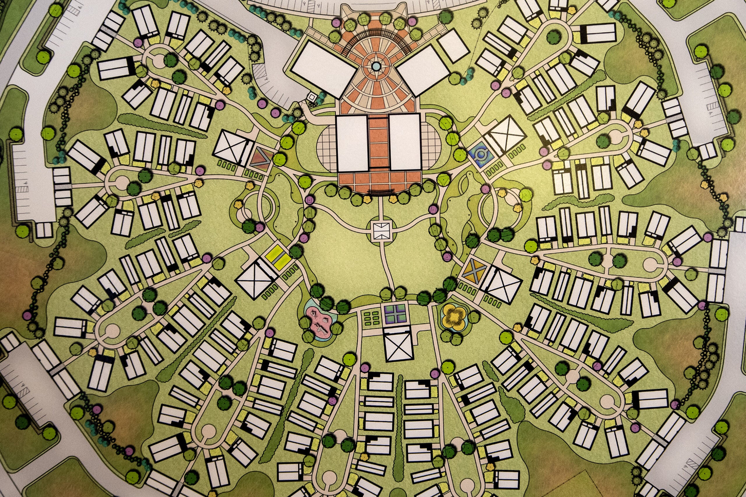 A detailed site plan of a residential community, showing clustered housing units, circular roads, pathways, green spaces, and central communal buildings.