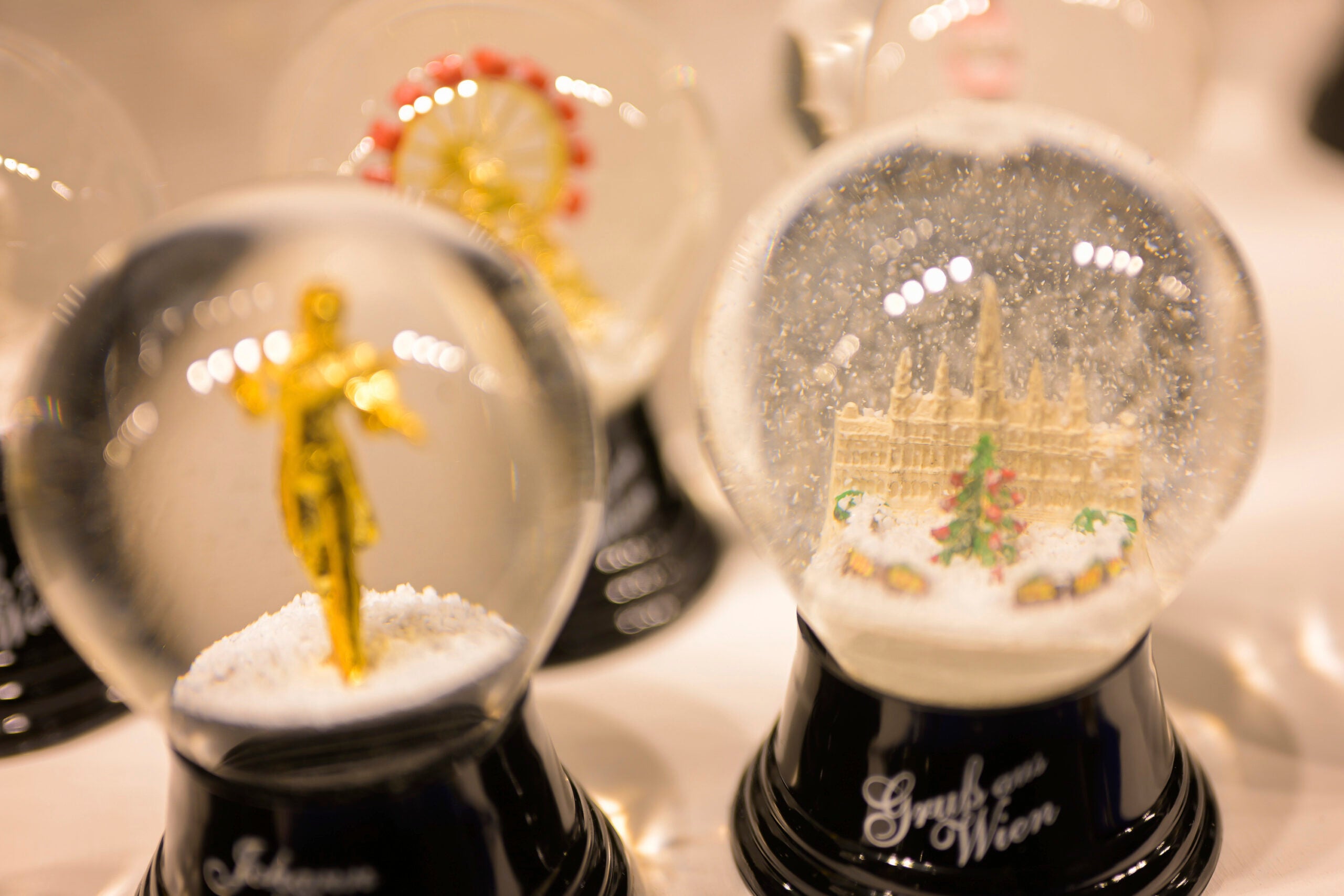 Several snow globes are displayed, including one with a golden statue and another with a detailed building and Christmas tree inside, both labeled with Gruß aus Wien.