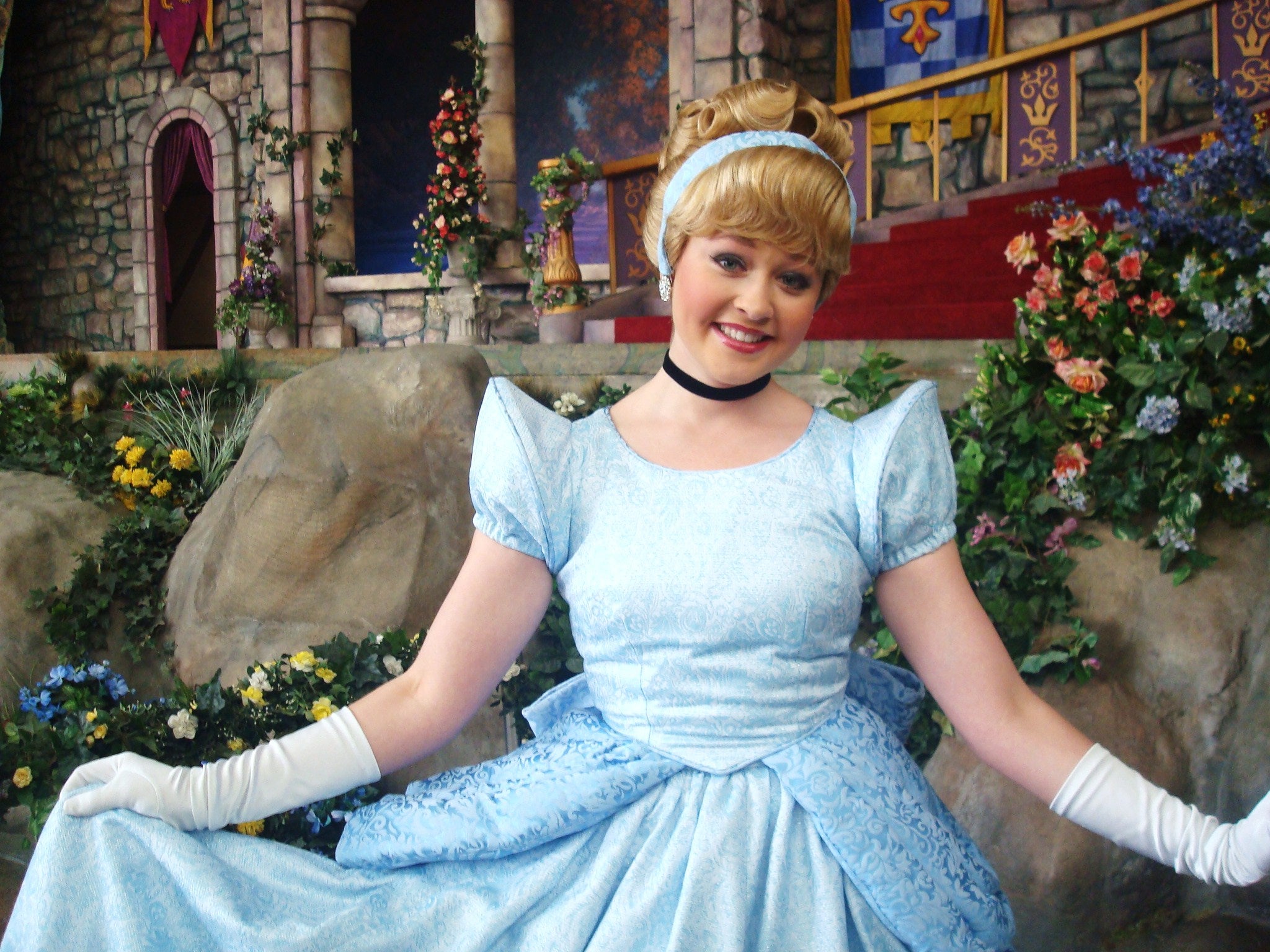 A woman dressed as Cinderella poses in front of a castle set decorated with flowers and stonework.
