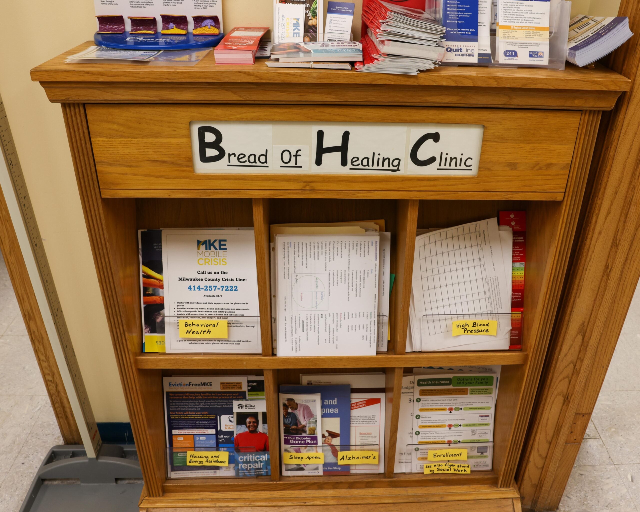 A wooden shelf labeled Bread of Healing Clinic holds brochures, pamphlets, and informational materials about health and community resources.
