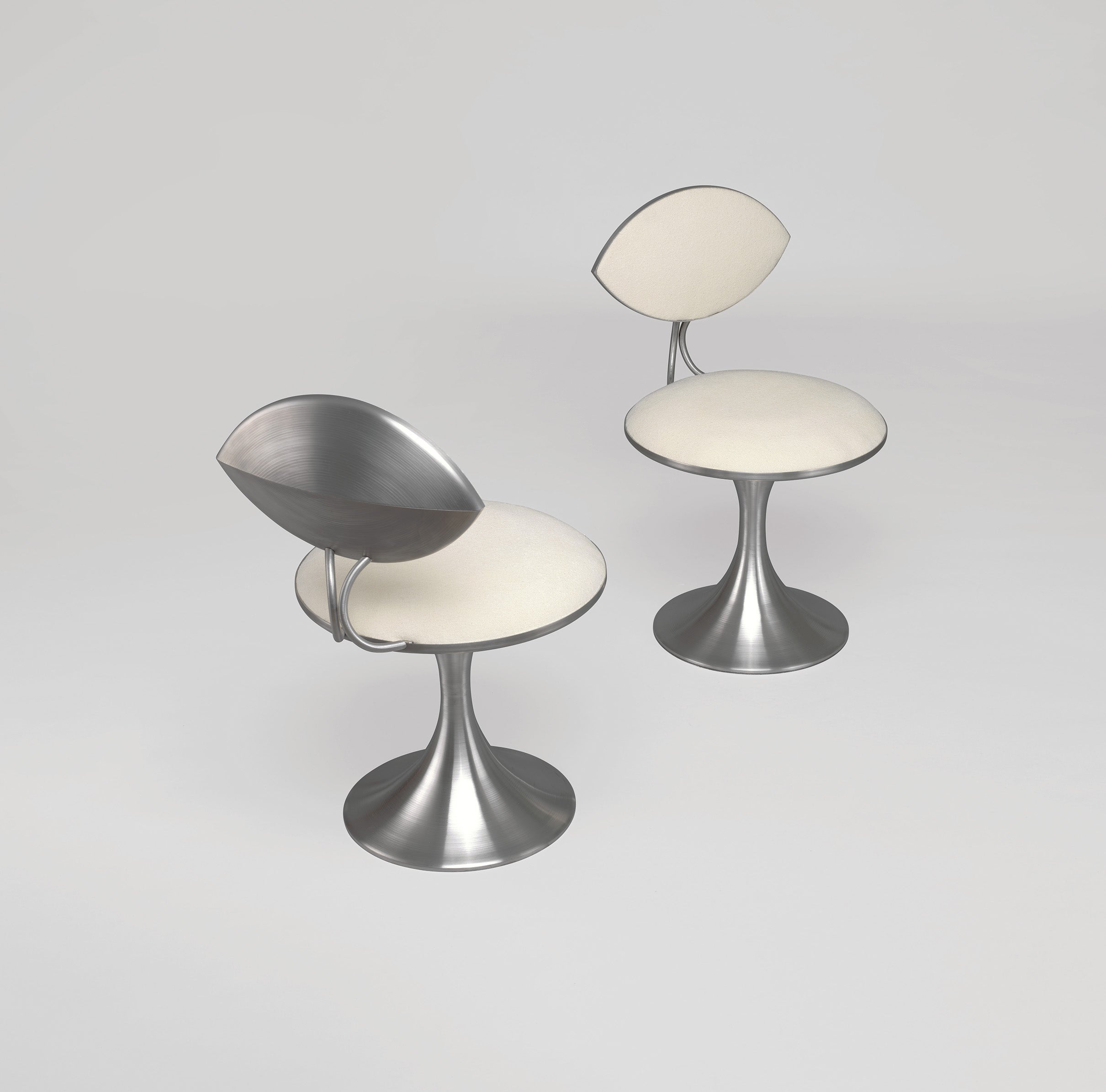 Two modern metal chairs with white cushioned seats and backs, featuring curved pedestal bases, are positioned on a plain light background.