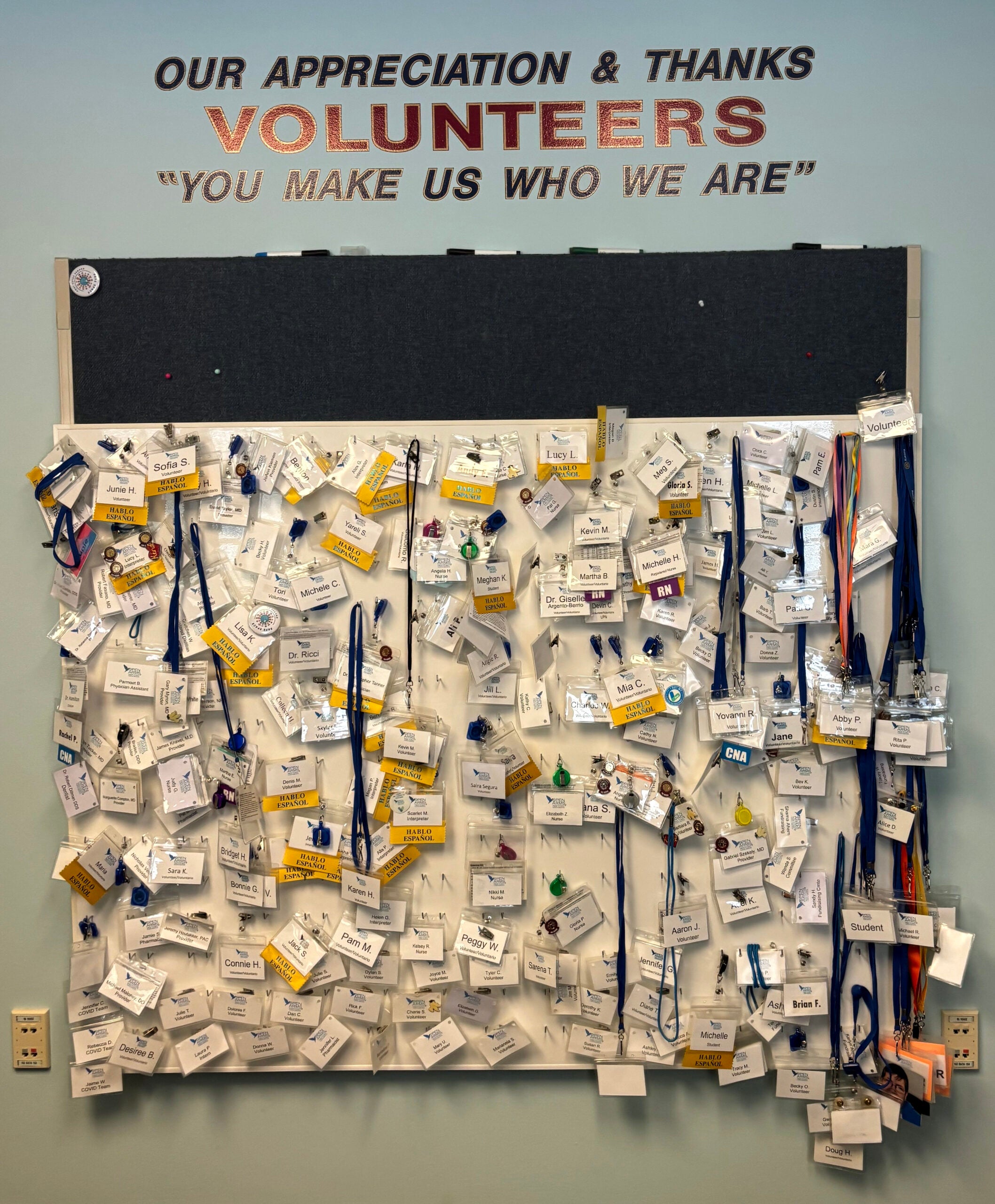 A bulletin board covered with many name badges and lanyards beneath a sign reading Our Appreciation & Thanks Volunteers You make us who we are.