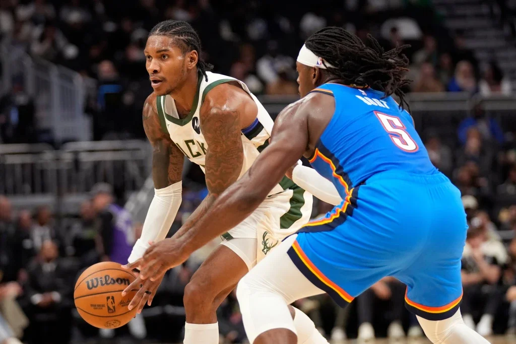 A basketball player in a white and green uniform dribbles while being guarded by a player in a blue uniform during a game.