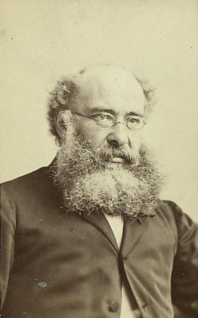 A bearded man with glasses and a receding hairline, wearing a dark jacket and white shirt, looks slightly past the camera in a sepia-toned portrait.