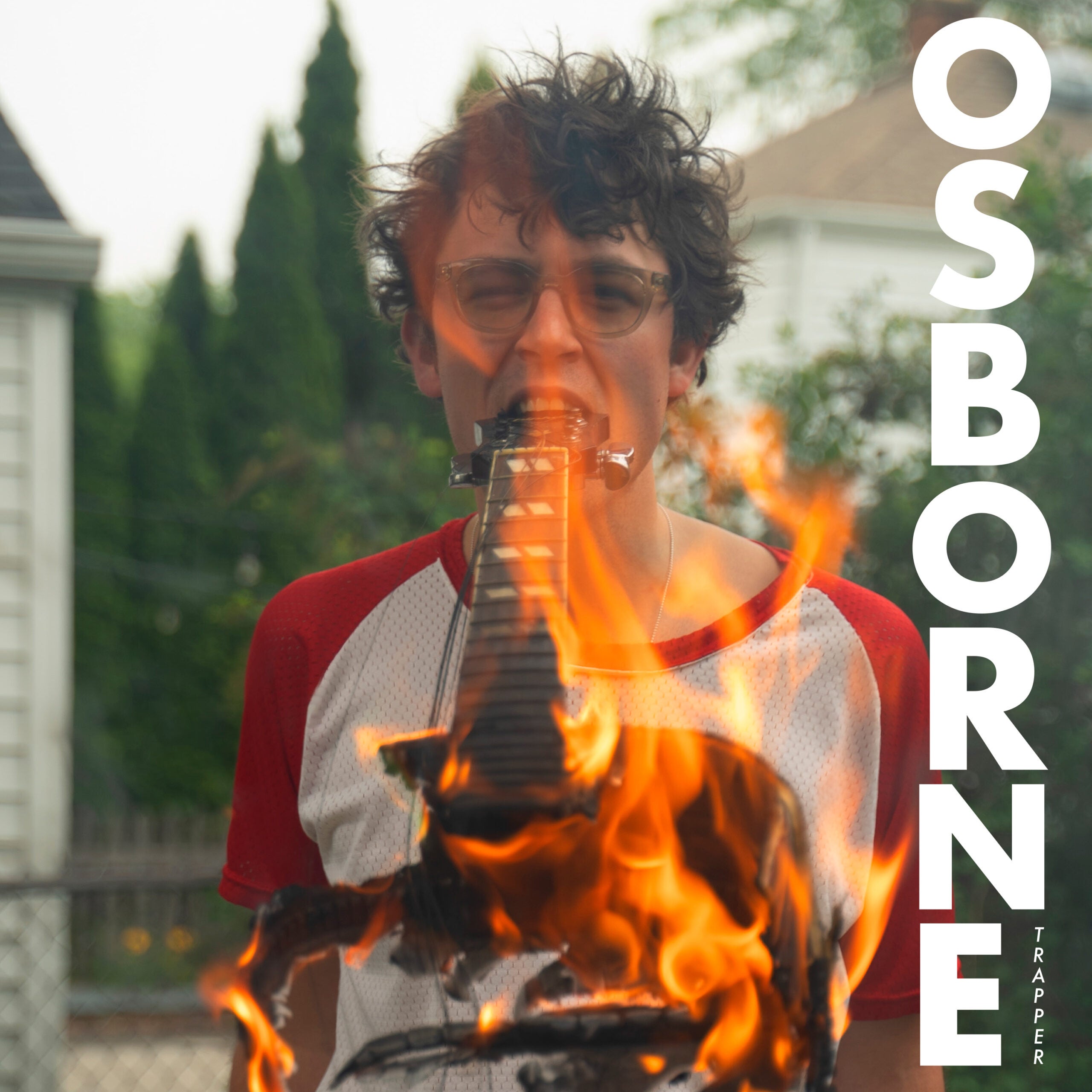 A person with glasses and a harmonica holder stands outdoors as flames obscure the lower part of the image. The word OSBORNE is written vertically on the right side.
