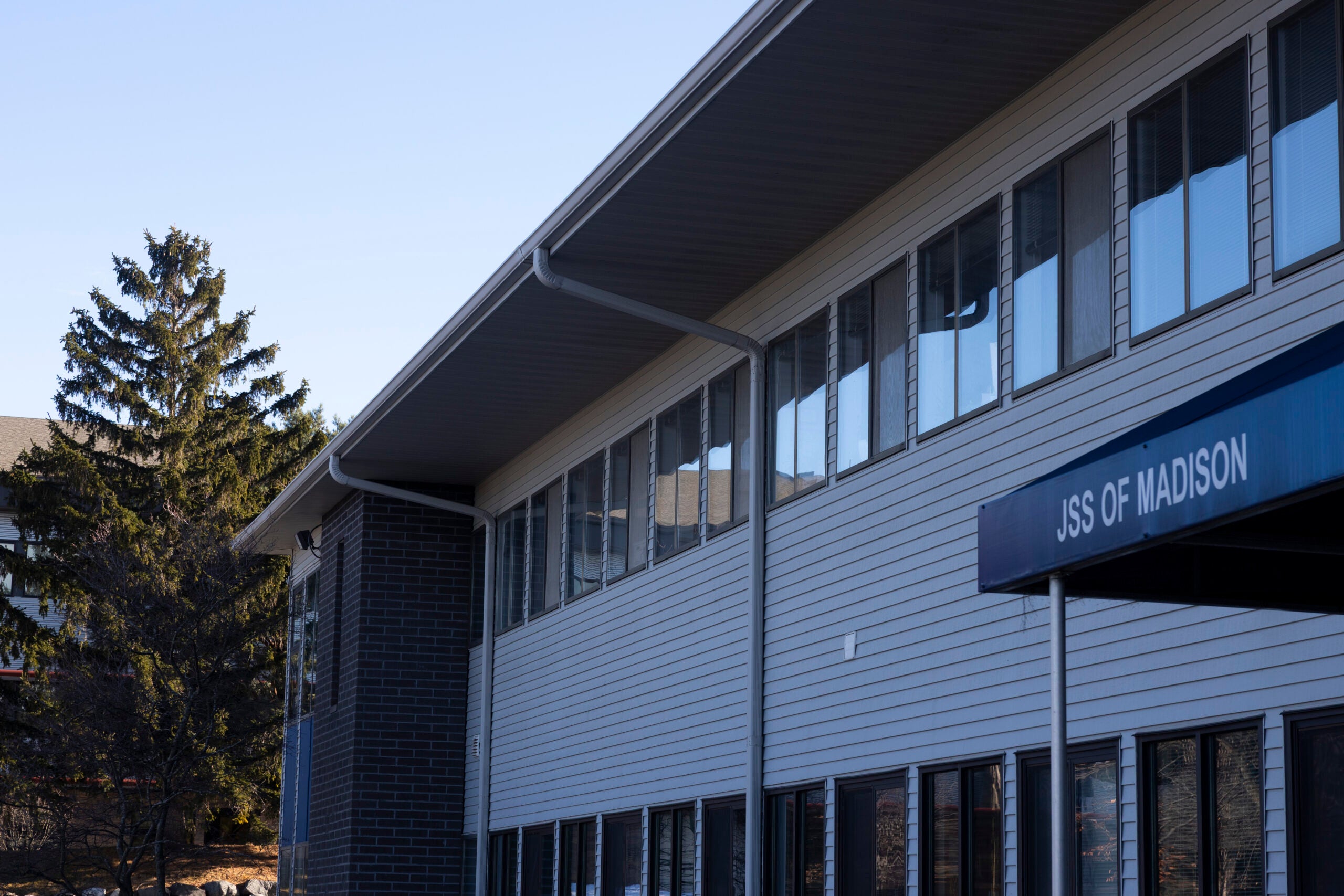 A two-story building with large windows and a sign reading JSS OF MADISON above the entrance, with trees visible in the background.