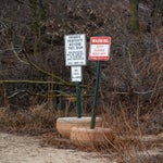 Two signs at the edge of a sandy area warn of private property, no pets allowed, and a closed jetty with instructions not to trespass. Leafless trees and bushes are in the background.