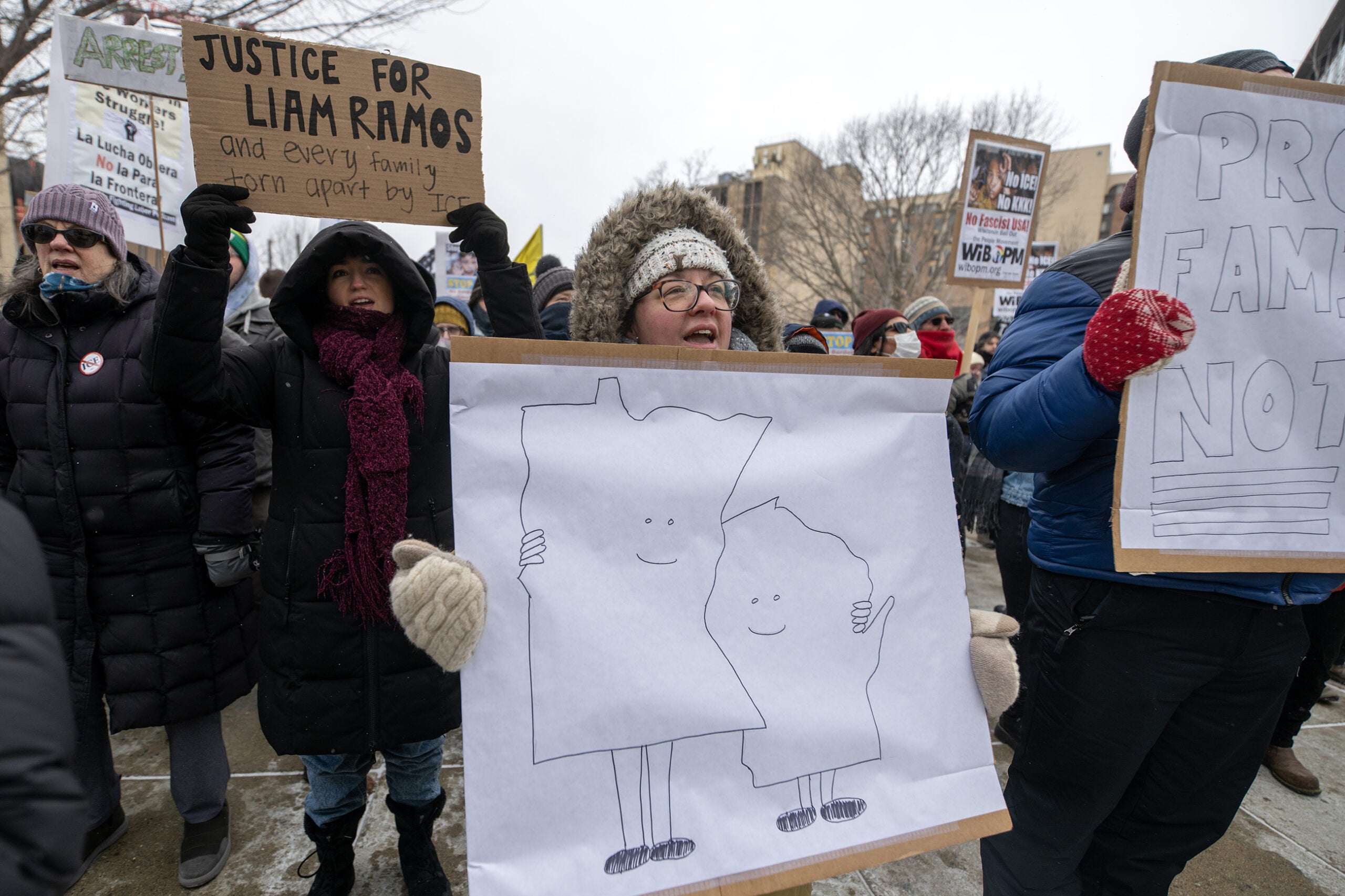A group of protesters bundled in winter clothing hold signs, including one with cartoon drawings of two U.S. states hugging and another reading Justice for Liam Ramos.