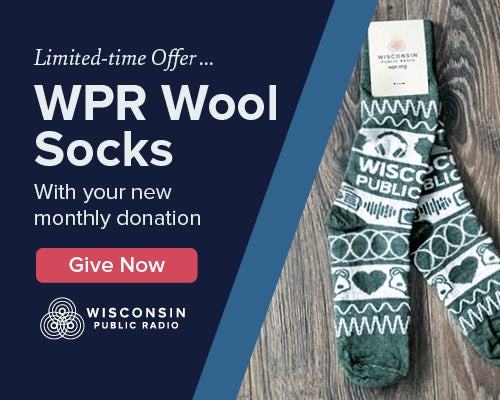 Pair of green and white Wisconsin Public Radio wool socks on a wooden surface, with text offering them for a new monthly donation.