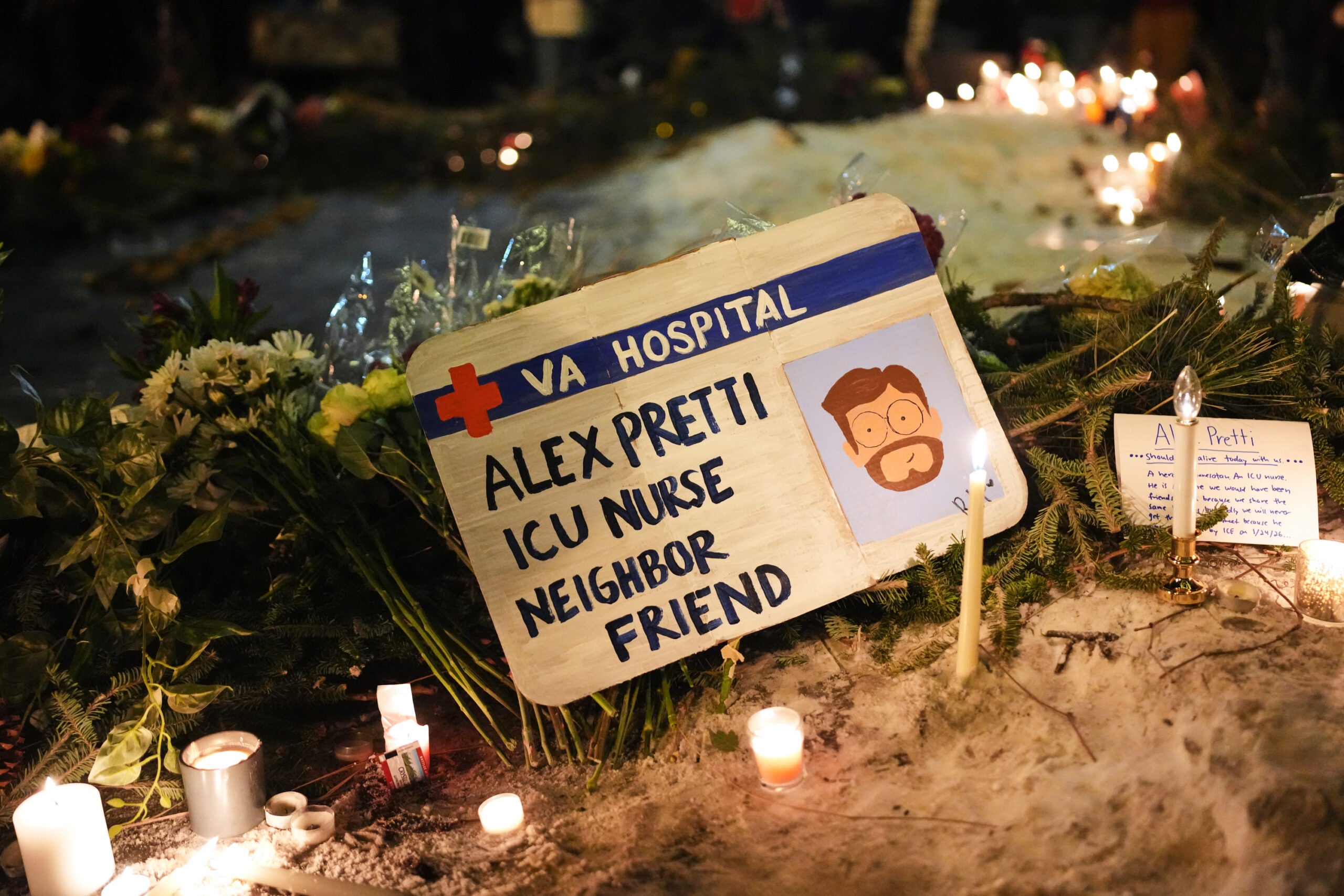 A memorial display with candles, flowers, and a sign for Alex Pretti, ICU nurse, neighbor, and friend, at VA hospital, surrounded by handwritten notes and lit candles at night.