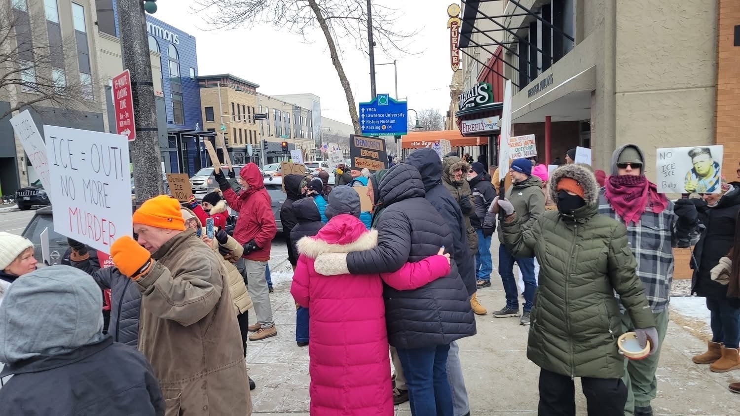 A group of people bundled in winter clothing hold signs and protest on a snowy city sidewalk.