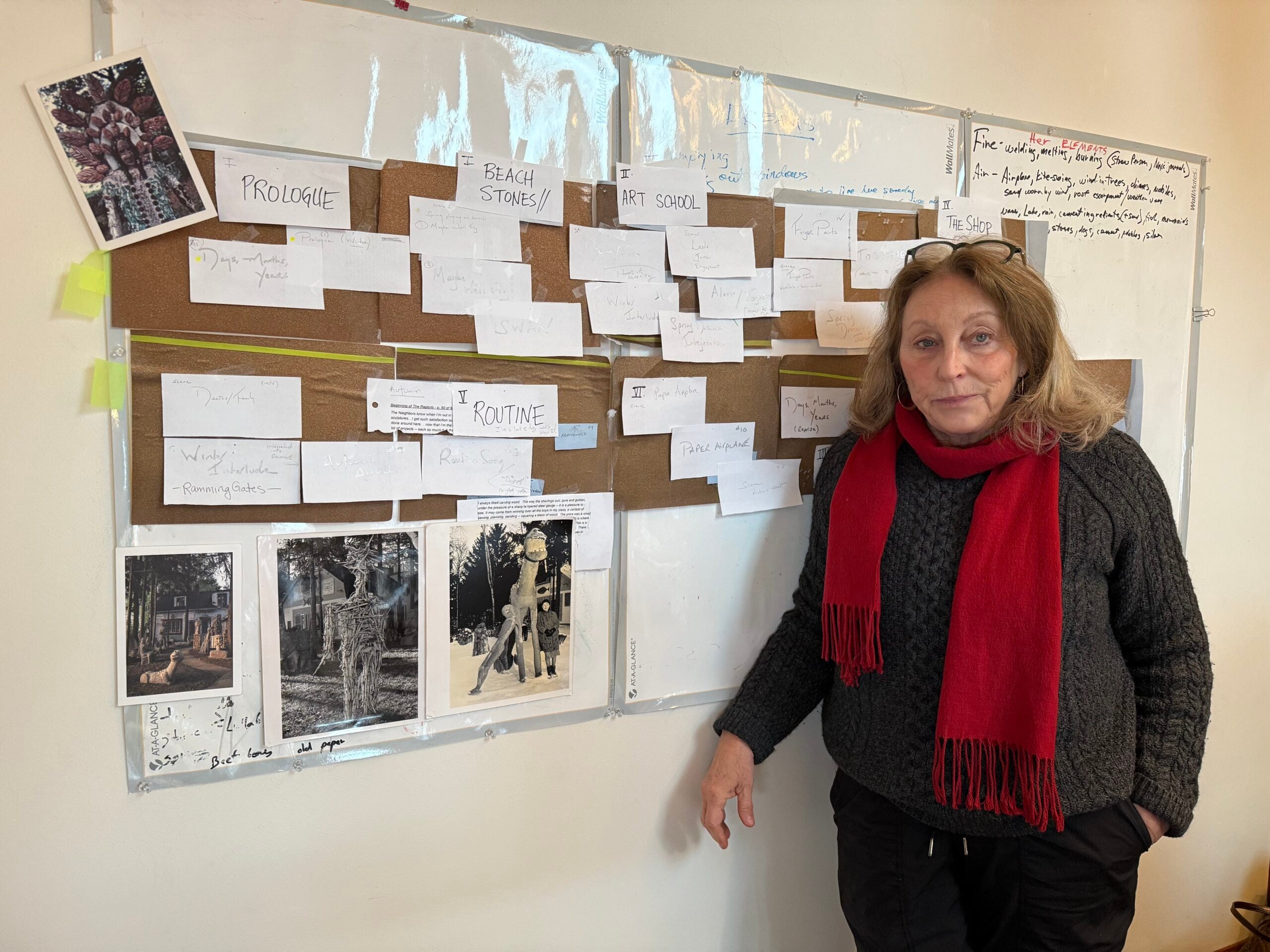 A woman in a red scarf stands by a whiteboard with index cards and photos, which appear to outline a project or storyline.
