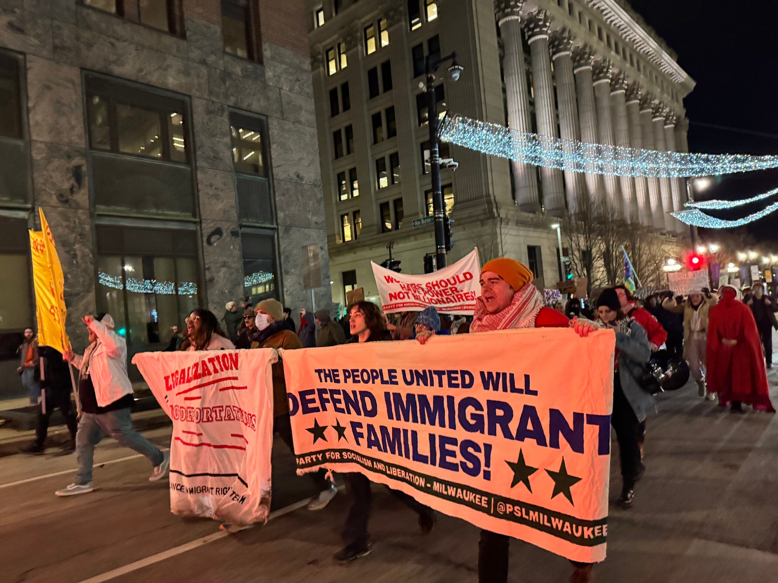 A group of people march down a city street at night holding banners that support immigrant families and call for legalization.