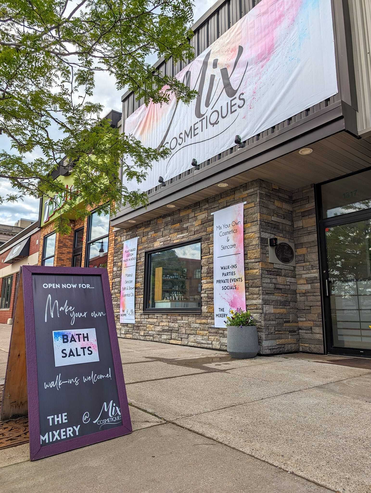 Storefront of Mix Cosmetiques with a sidewalk sign advertising Make your own bath salts and banners promoting custom cosmetics and walk-ins.