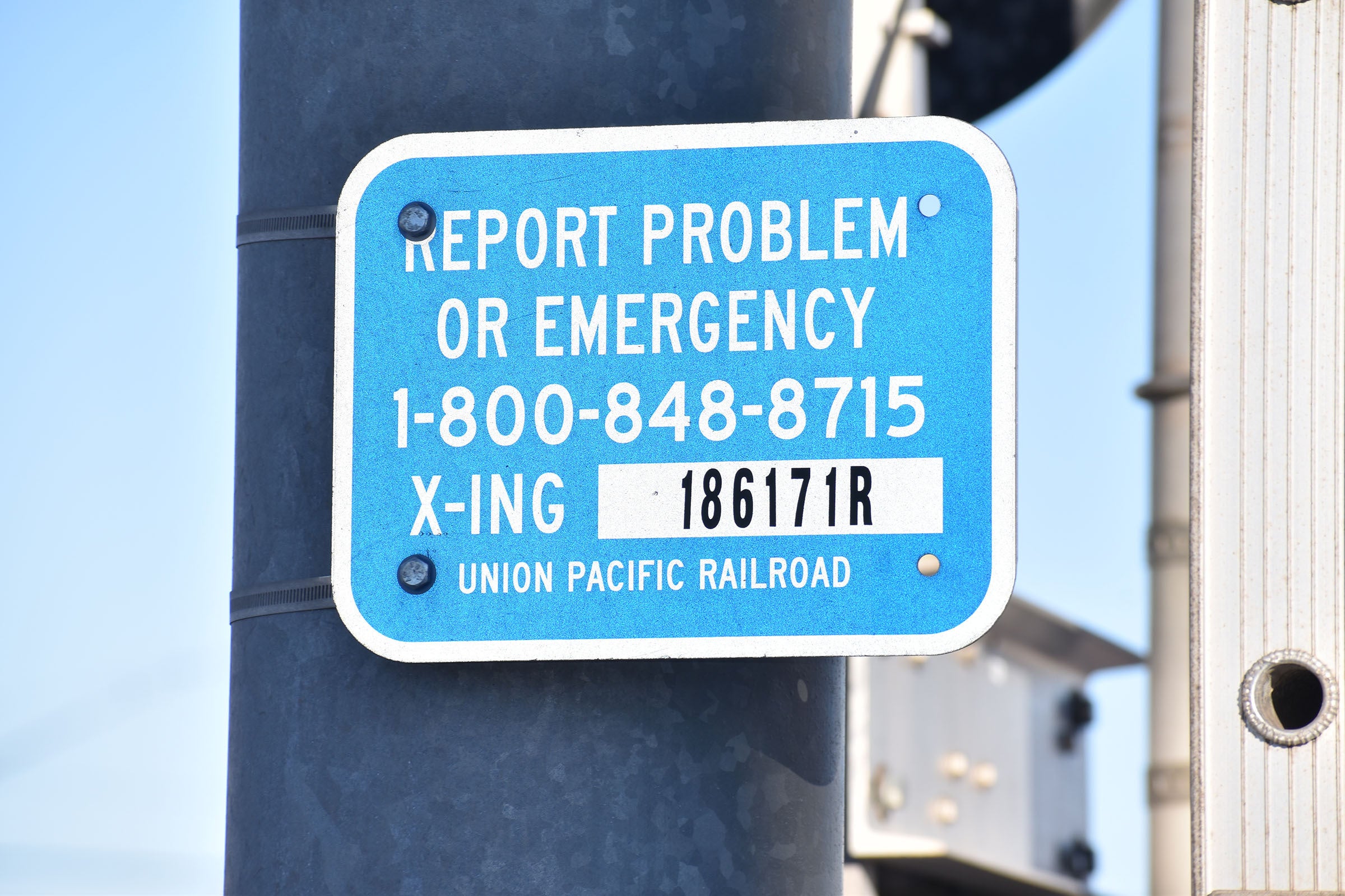 Blue and white Union Pacific Railroad sign with a phone number for reporting problems or emergencies and crossing ID 186171R.