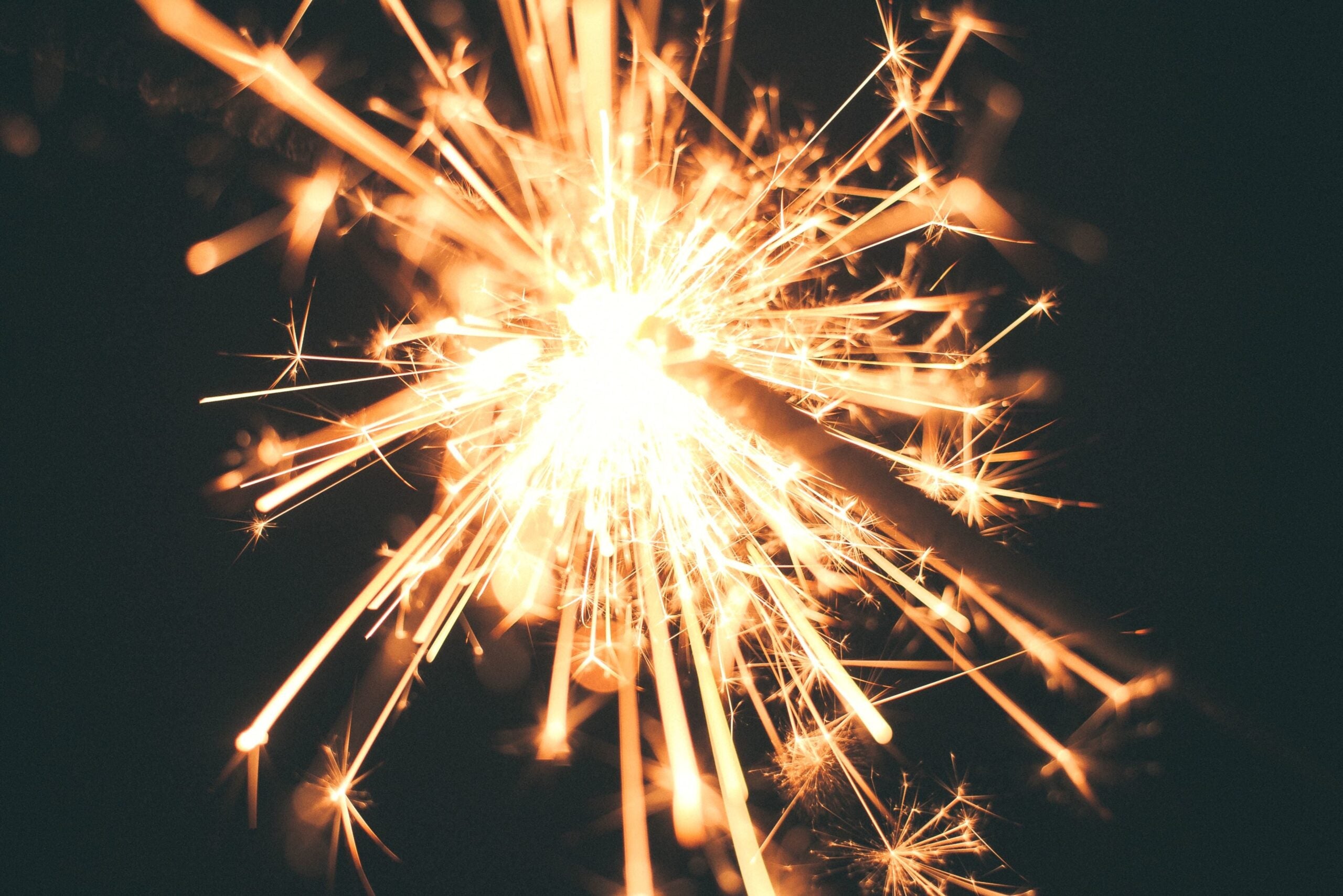 A close-up view of a lit sparkler with bright, glowing sparks against a dark background.