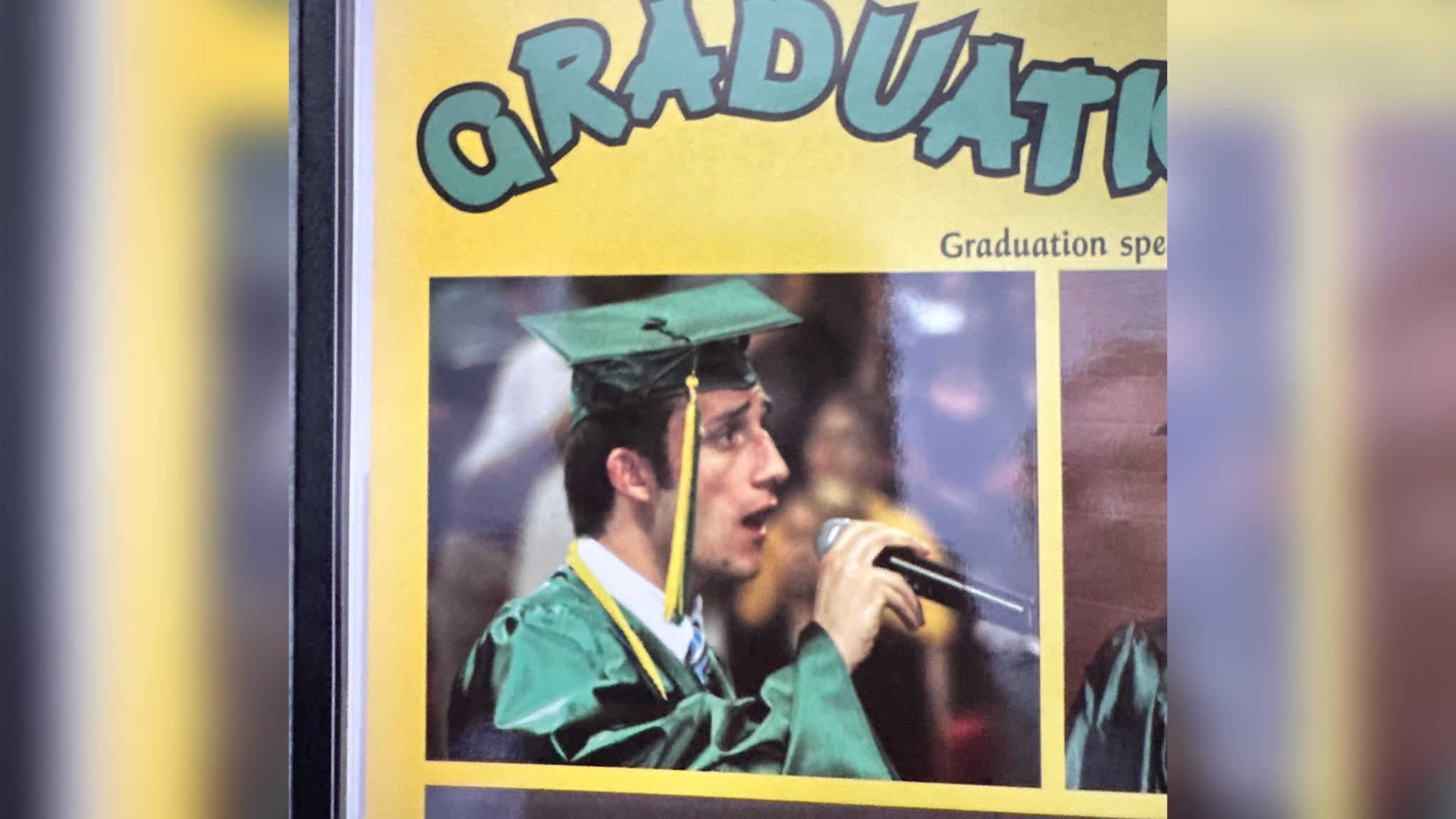 A student in a green graduation cap and gown speaks into a microphone during a graduation ceremony.